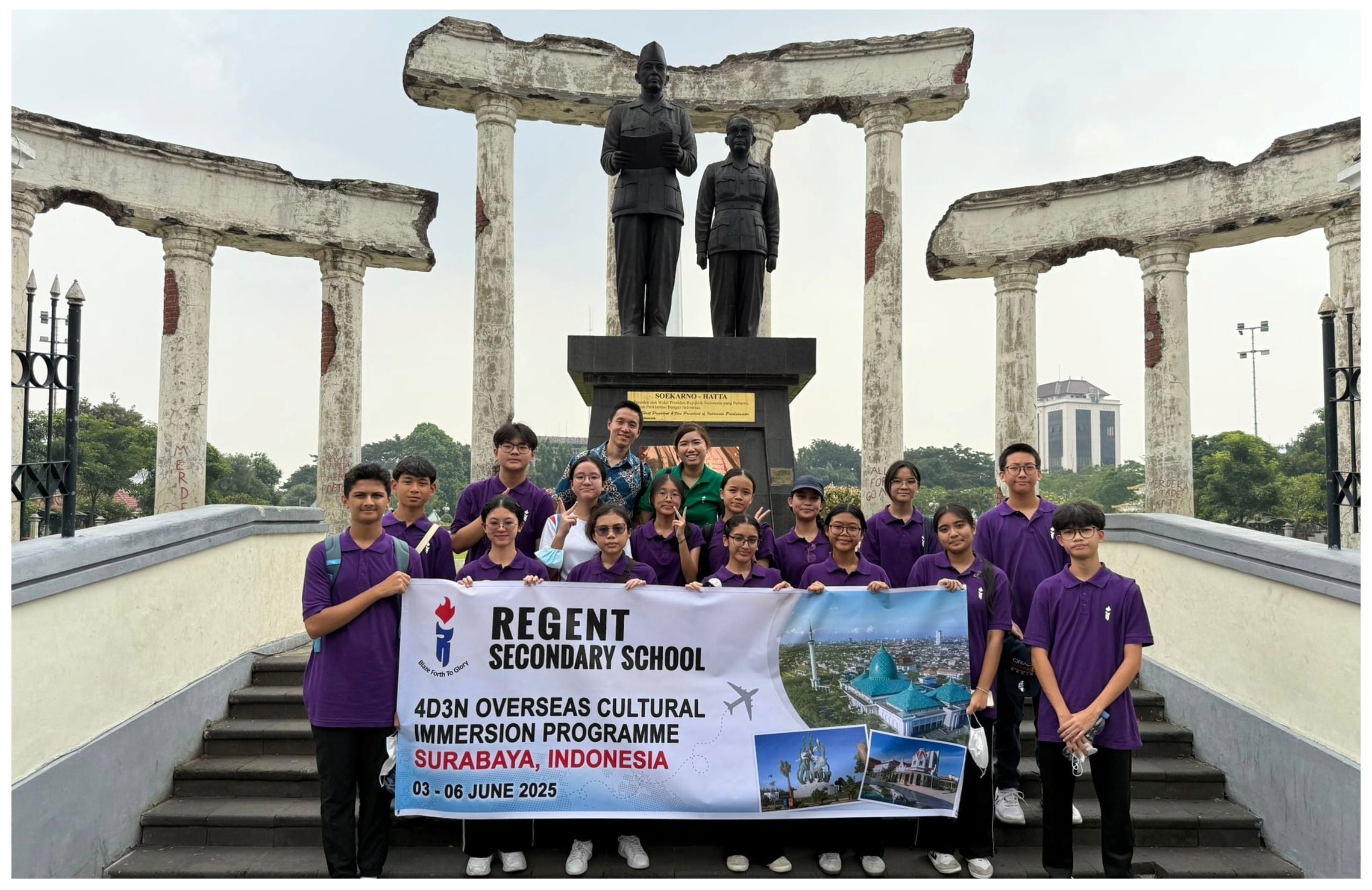 Students in purple uniforms hold a Regent Secondary School banner at the Soekarno-Hatta statue in Surabaya, Indonesia.