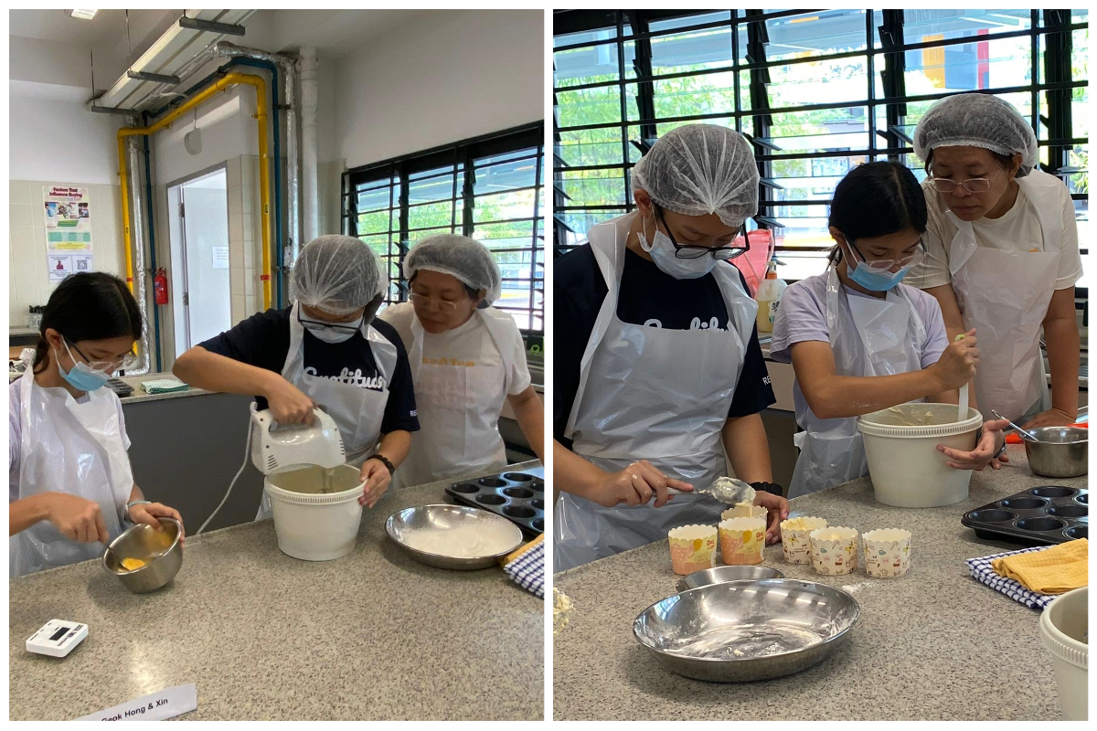 Three people wearing hairnets, aprons, and masks bake together, mixing batter and filling cupcake cups in a kitchen.