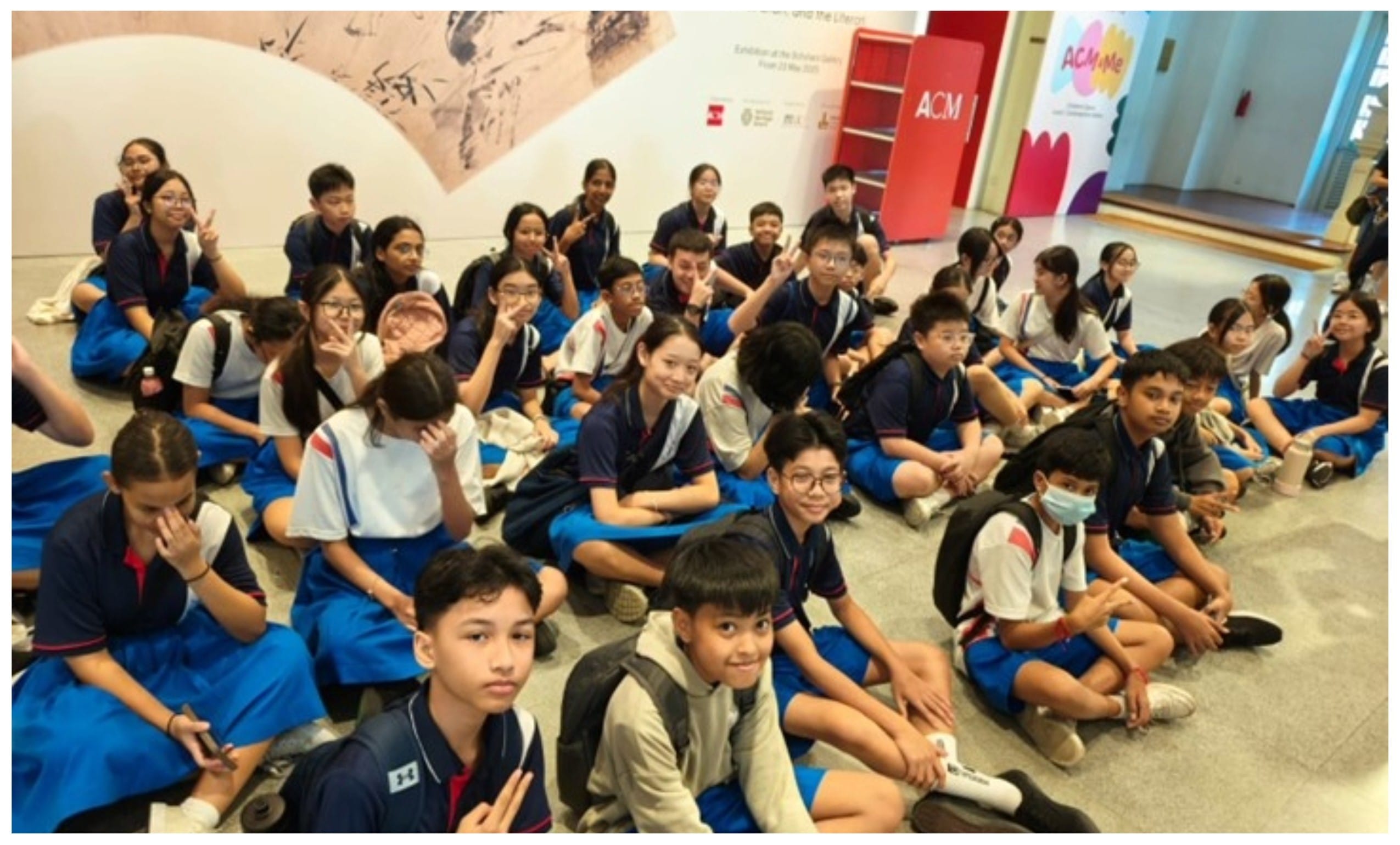 A large group of students in blue and white uniforms sitting on the floor inside the ACM museum.