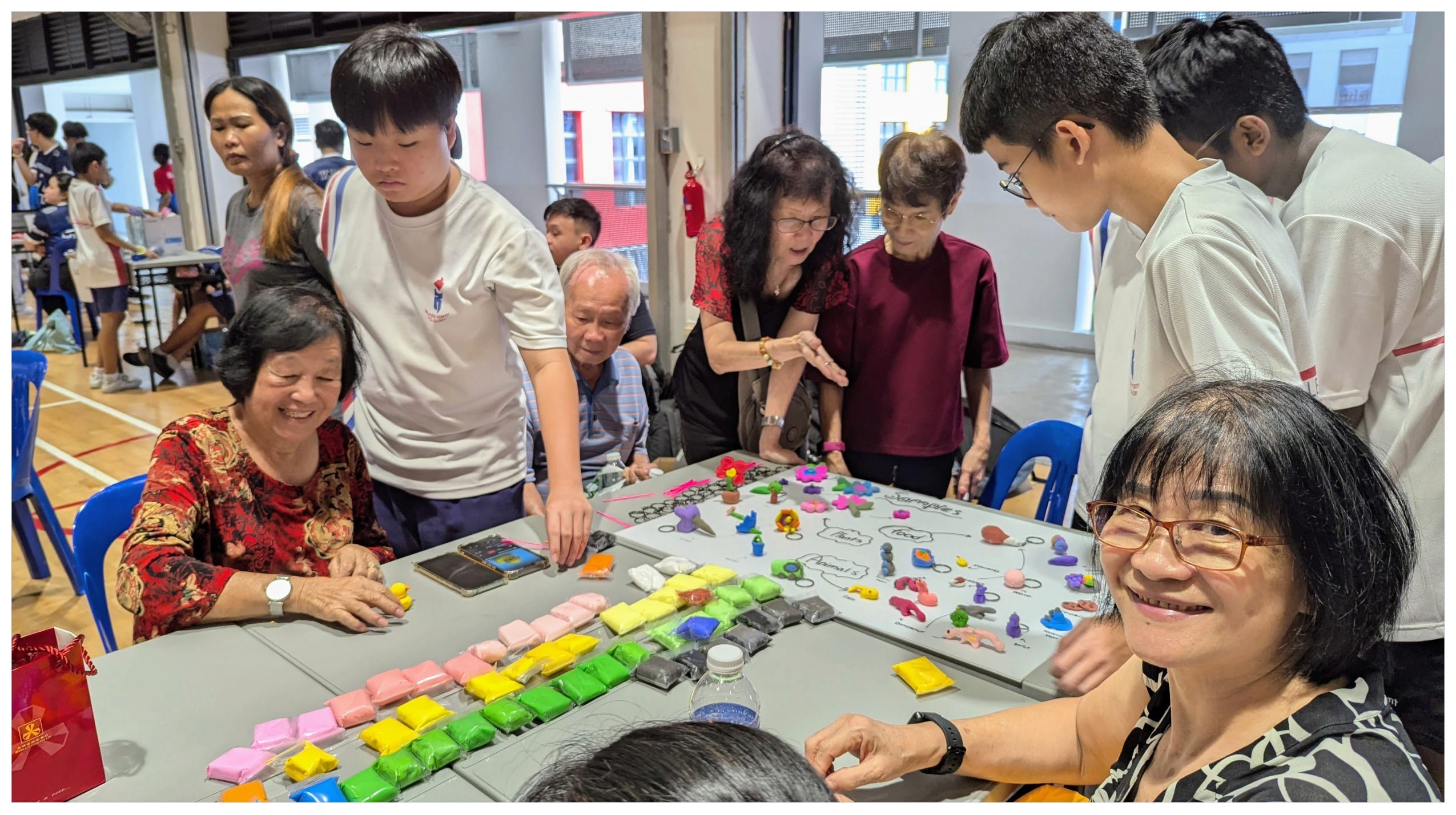 A group of adults and teens gather around a table with colorful clay blocks and small sculpted figures on a board.