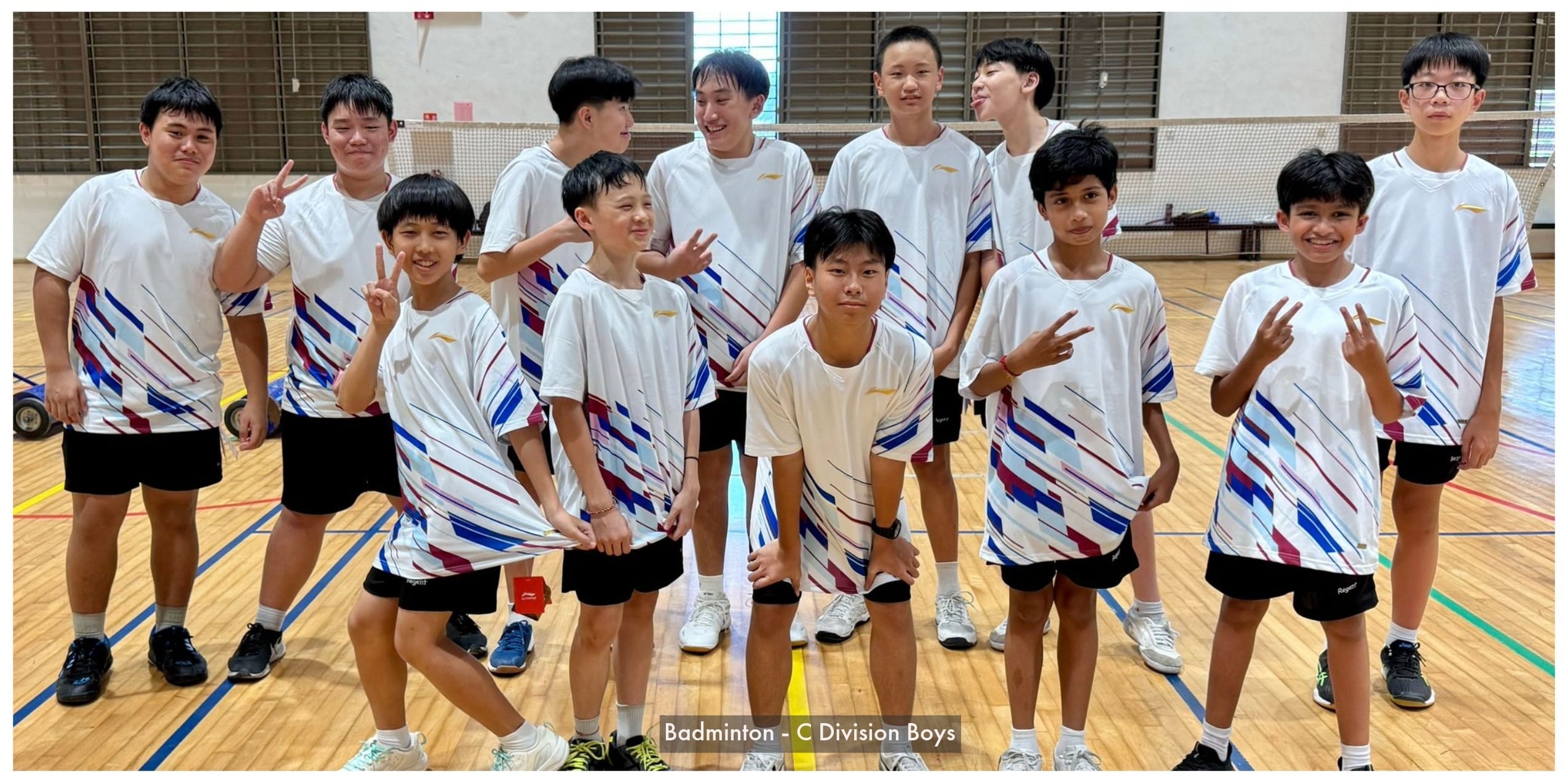 A group of young boys in matching white badminton uniforms pose together on an indoor court.