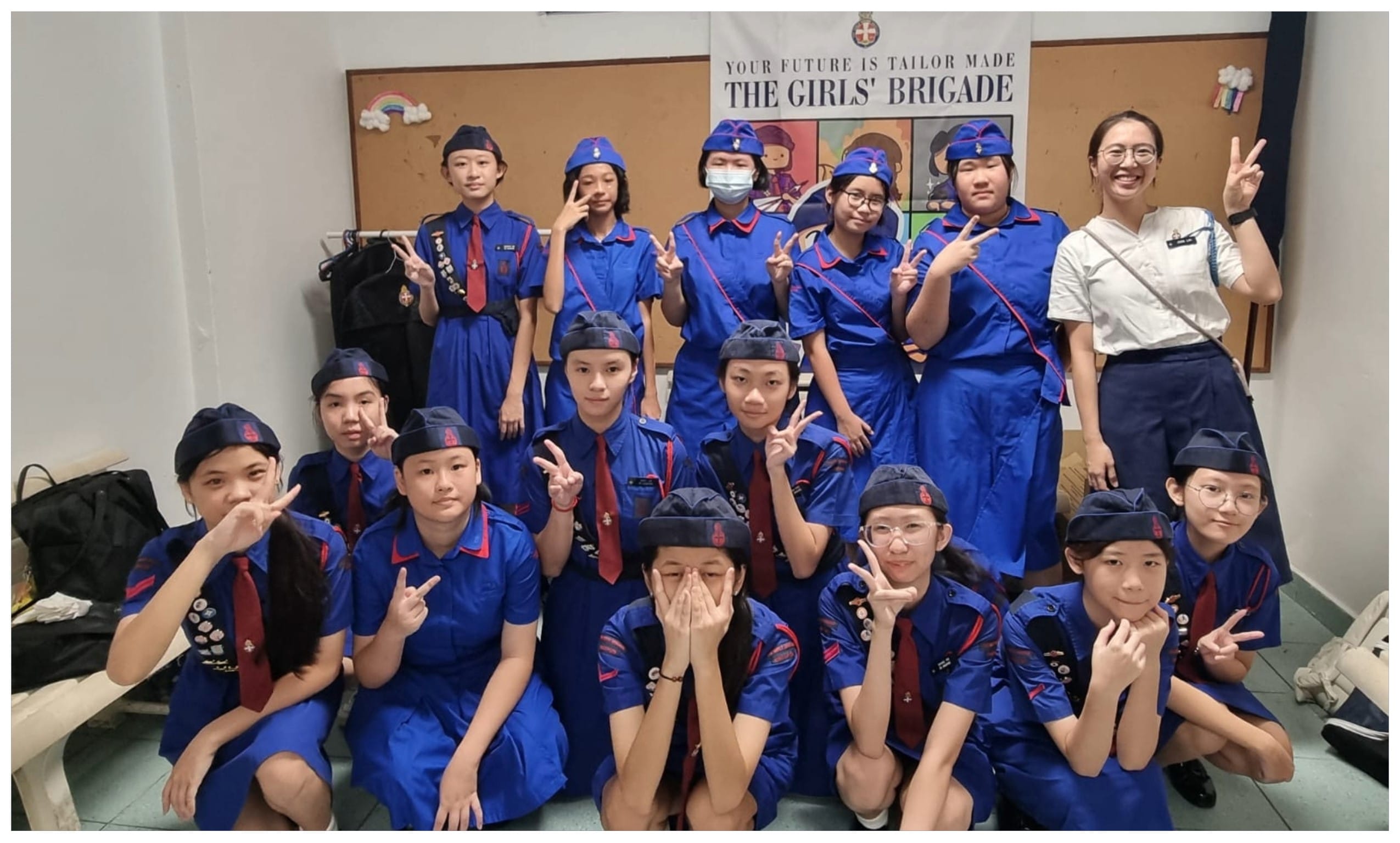 Group of young girls in blue Girls' Brigade uniforms posing with peace signs in front of a brigade banner.