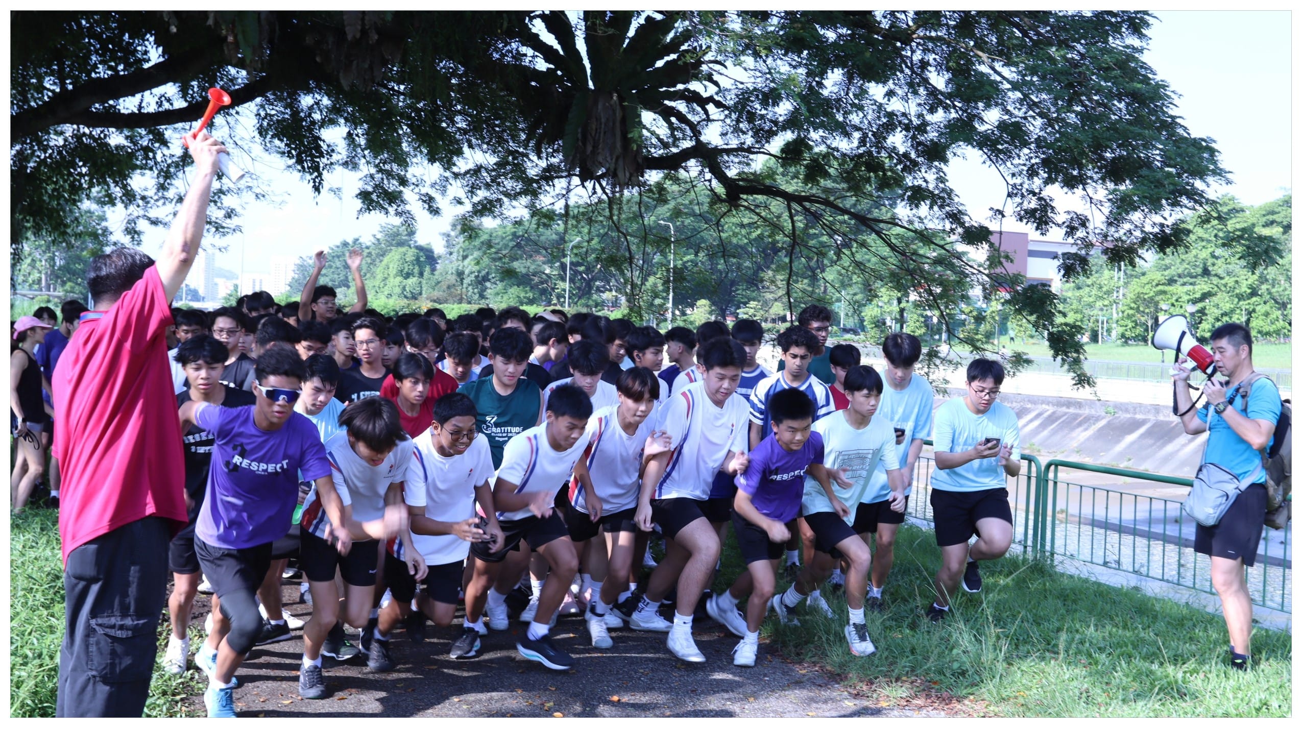 A large group of students starts a race as an official raises a horn and another holds a megaphone nearby.