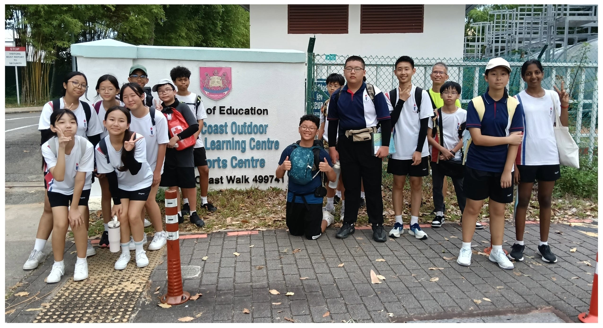 A group of students and an adult posing in front of a Coast Outdoor Learning Centre sign in Singapore.