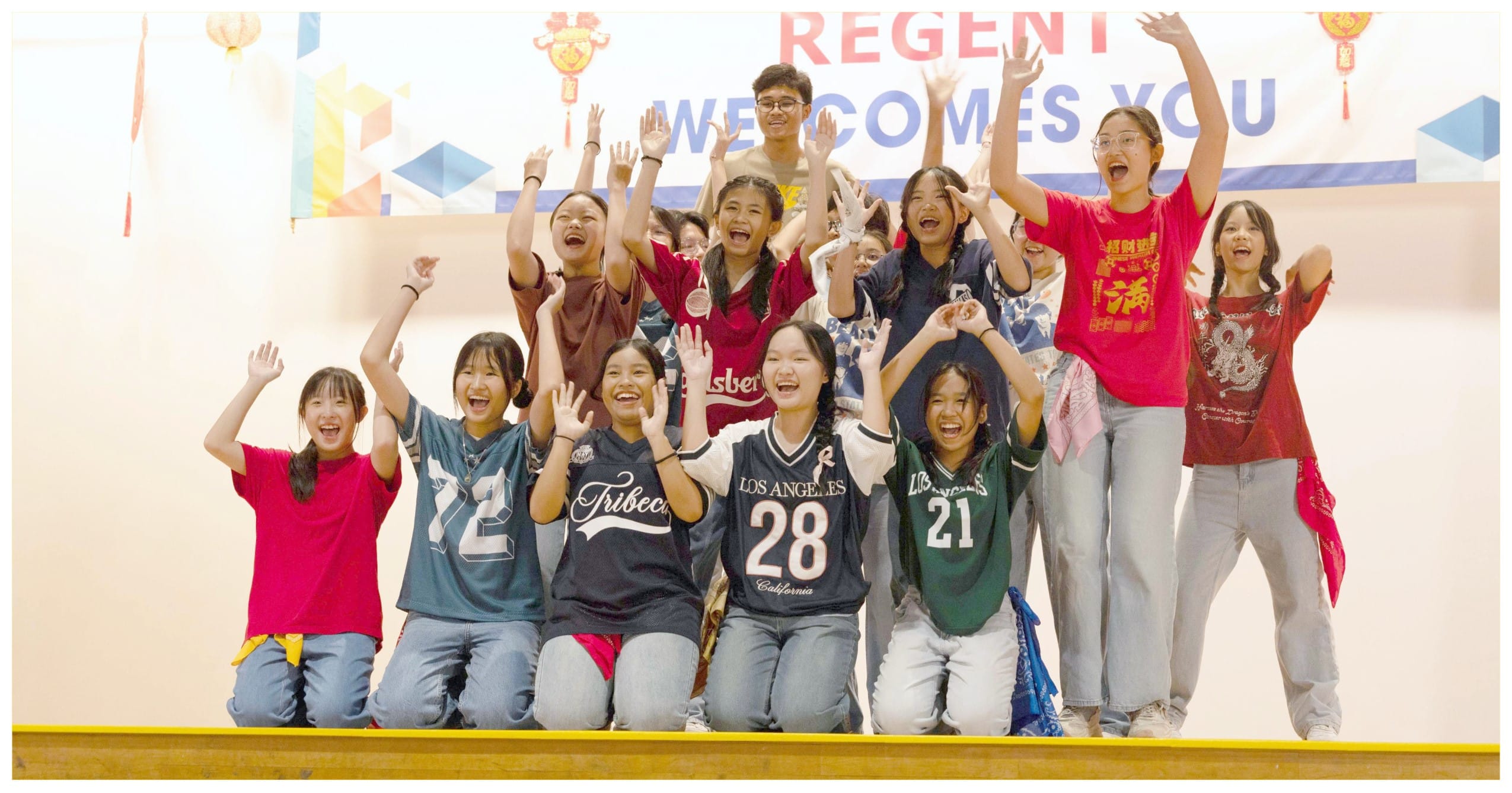A group of cheering students on a stage under a banner reading Regent Welcomes You.