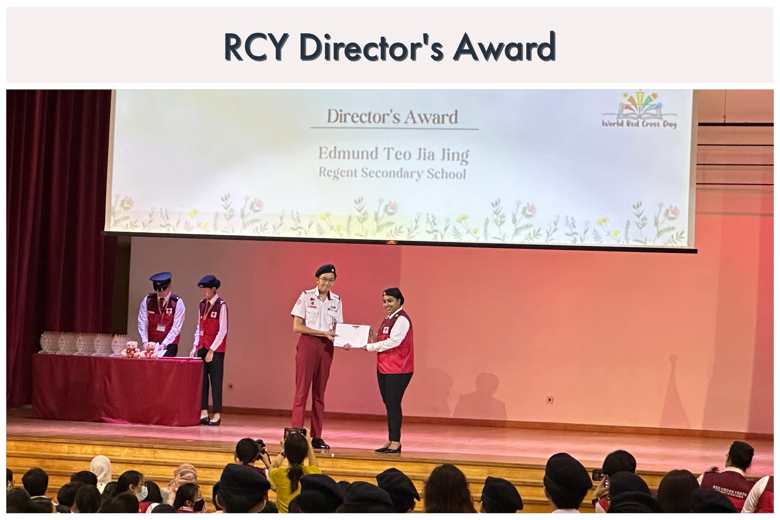 Two people in Red Cross uniforms exchange a certificate on stage at the RCY Director's Award ceremony.