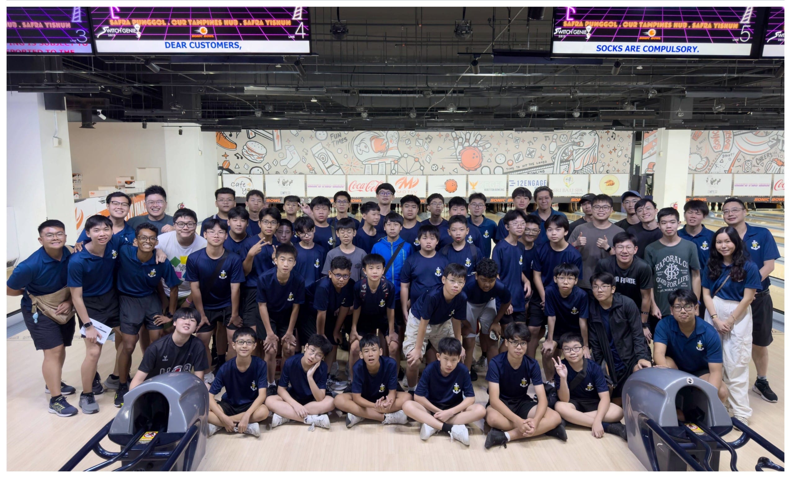 Large group of students in navy uniforms posing for a photo inside a bowling alley.