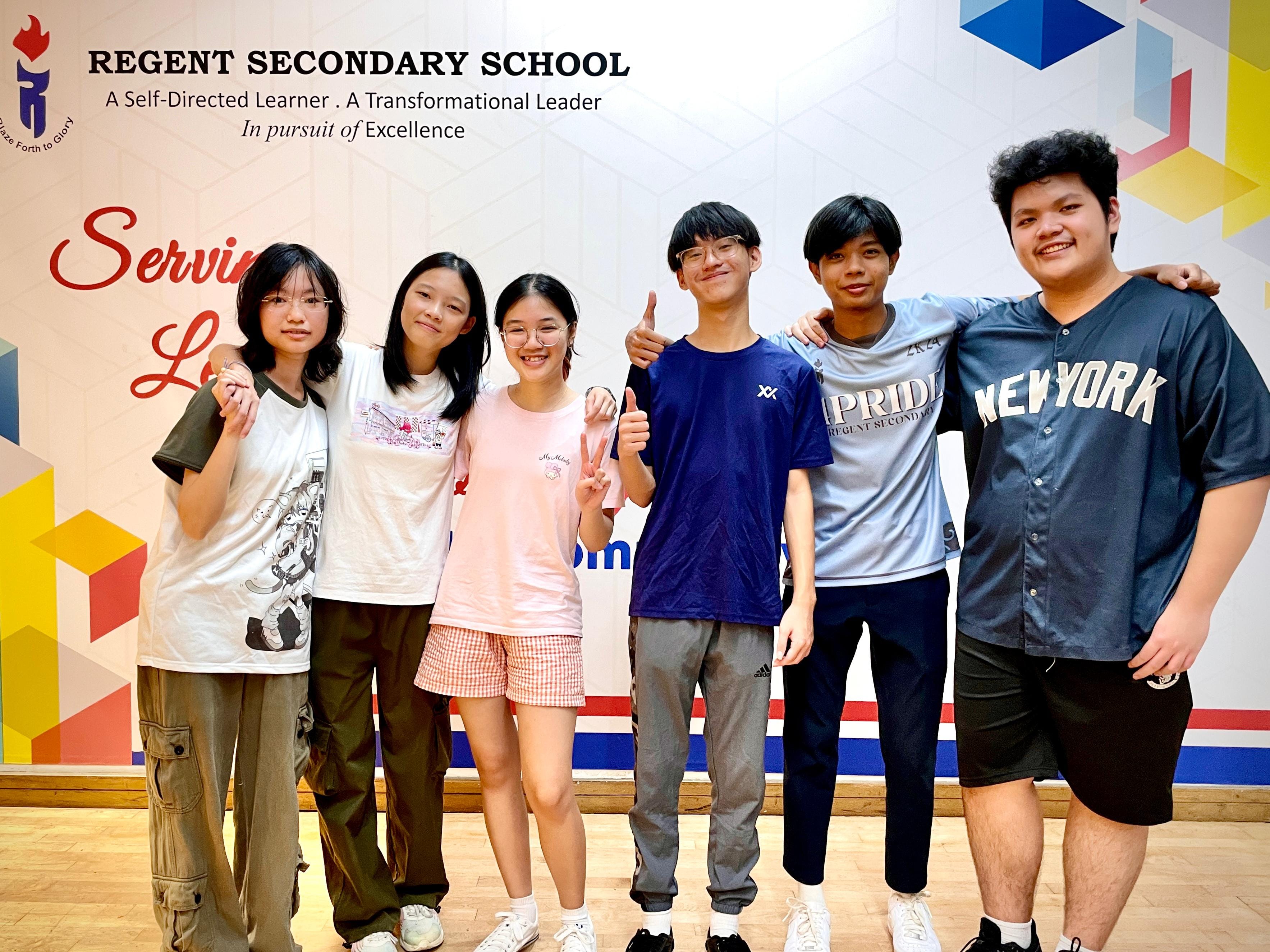 Six smiling students pose together in front of a Regent Secondary School banner.