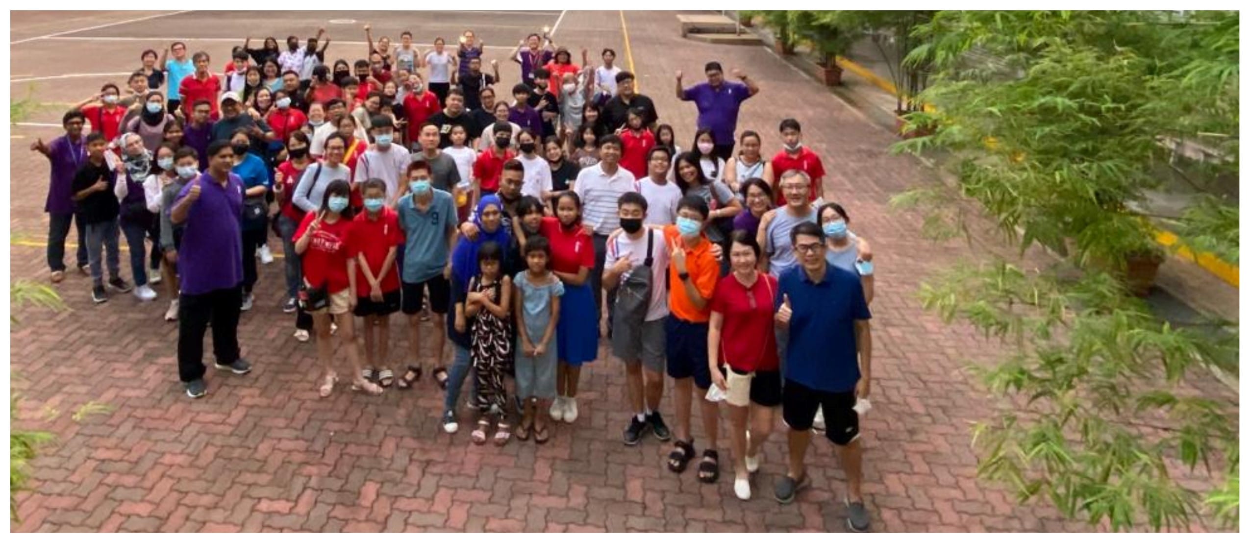 Large group of people wearing masks posing together on a brick courtyard, surrounded by trees.