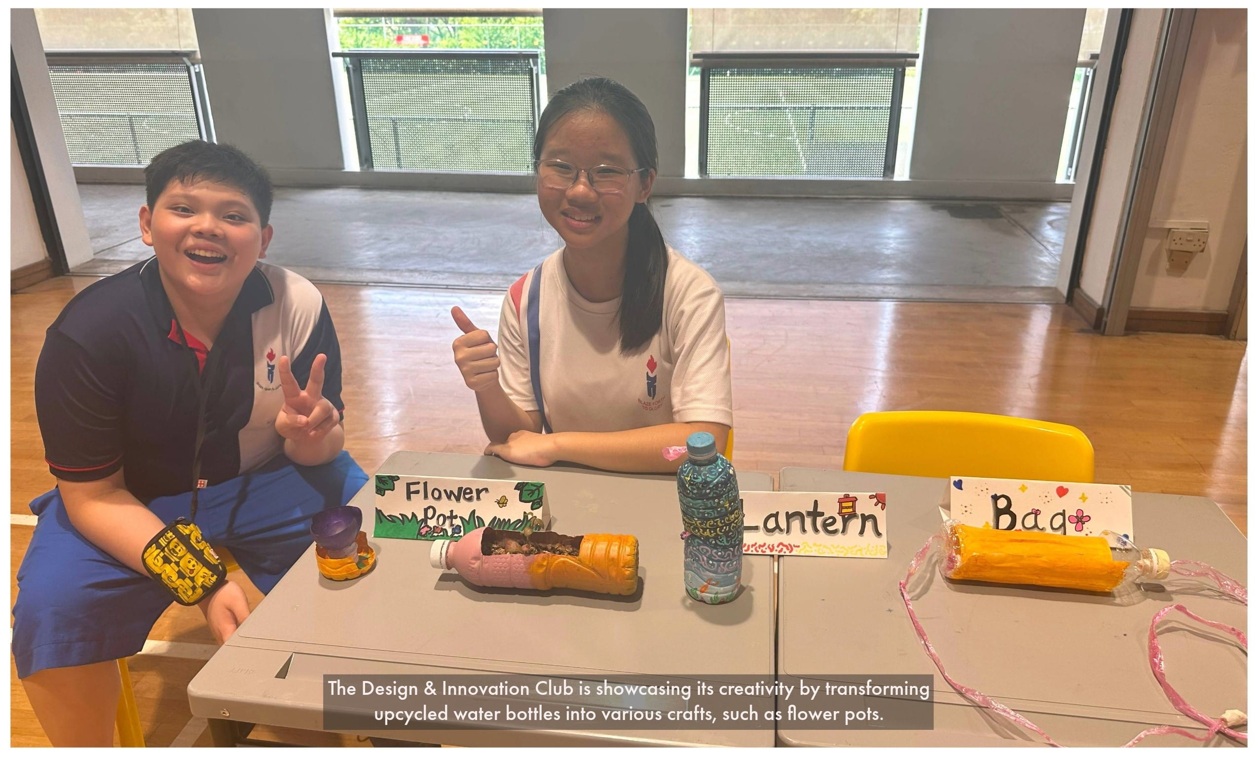 Two smiling students sit at a table displaying upcycled bottle crafts labeled Flower Pot, Lantern, and Bag.