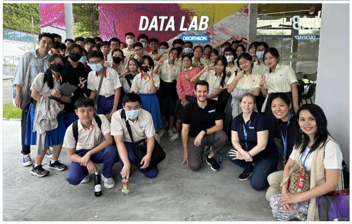 A large group of students in uniforms pose with staff in front of a Decathlon Data Lab sign.