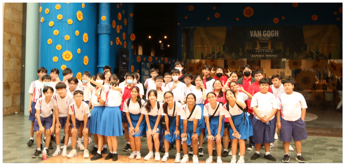 Students in school uniforms pose as a group outside a Van Gogh exhibition entrance decorated with sunflowers.