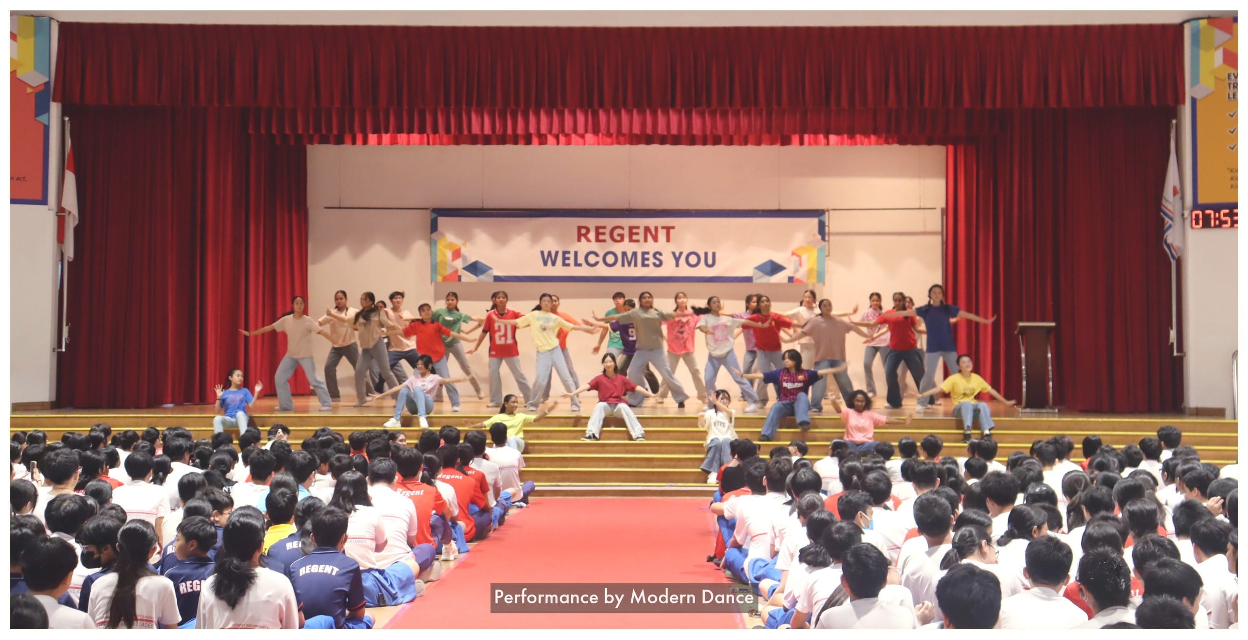 Students perform a modern dance on a stage with a red curtain and a banner reading Regent Welcomes You.