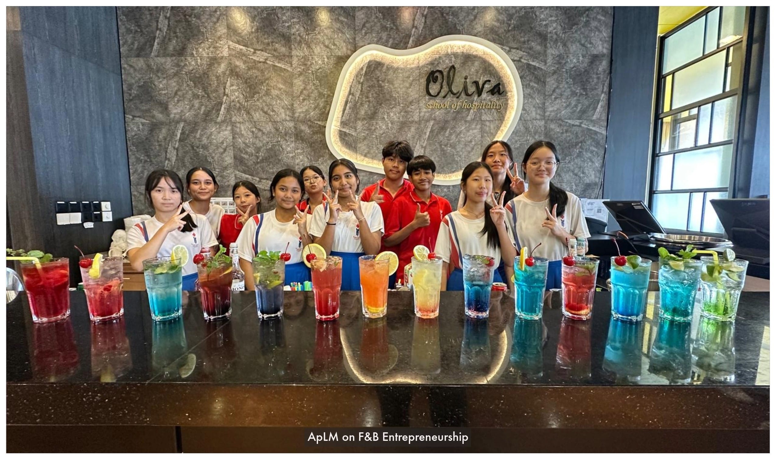 Students pose behind a bar counter with colorful drinks at Oliva School of Hospitality.
