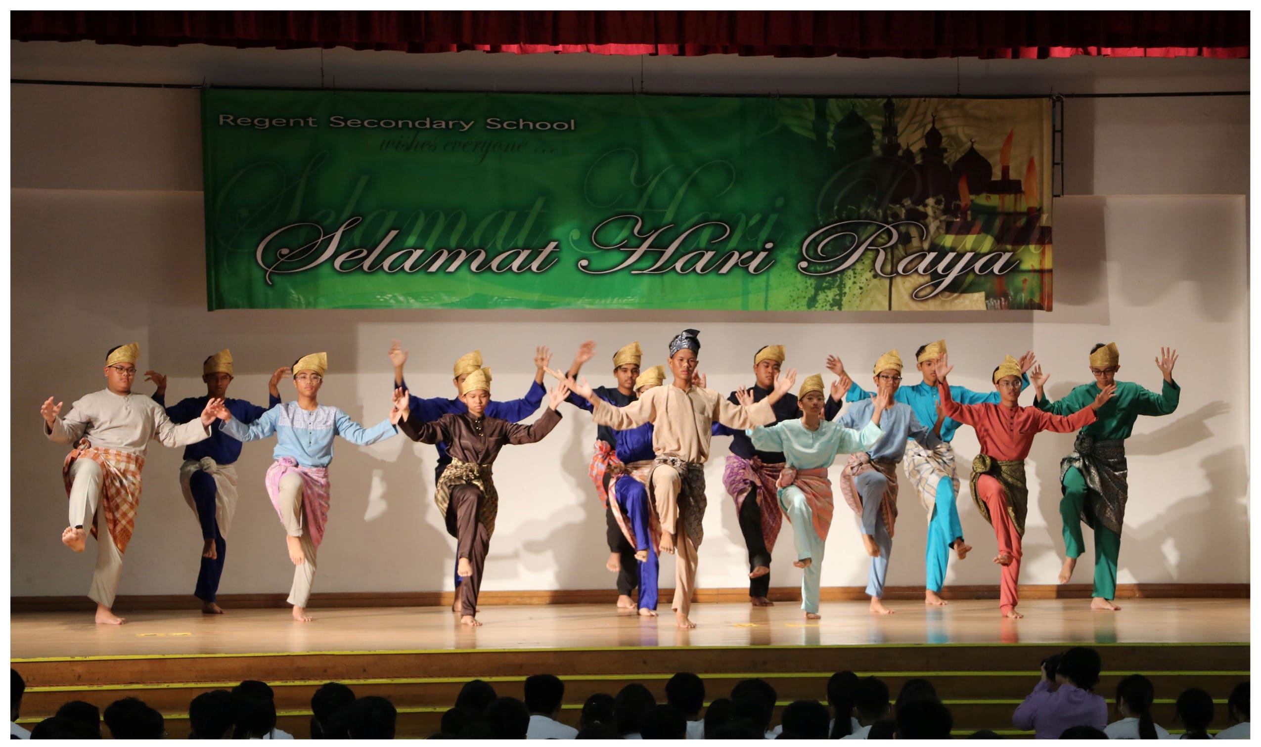 Students in traditional Malay costumes perform a dance on stage under a Selamat Hari Raya banner at Regent Secondary School.