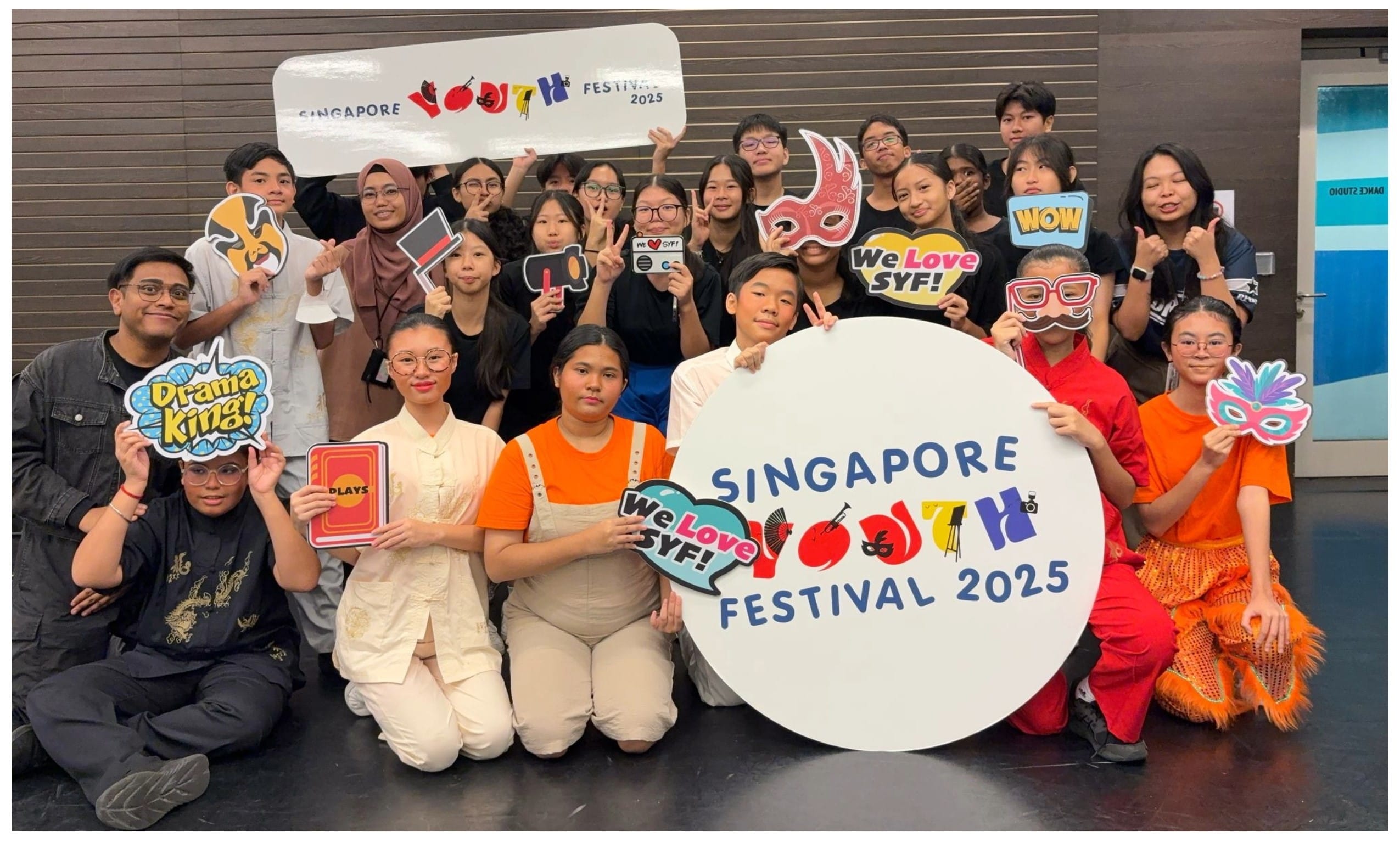 A large group of youths posing with props and signs for Singapore Youth Festival 2025.