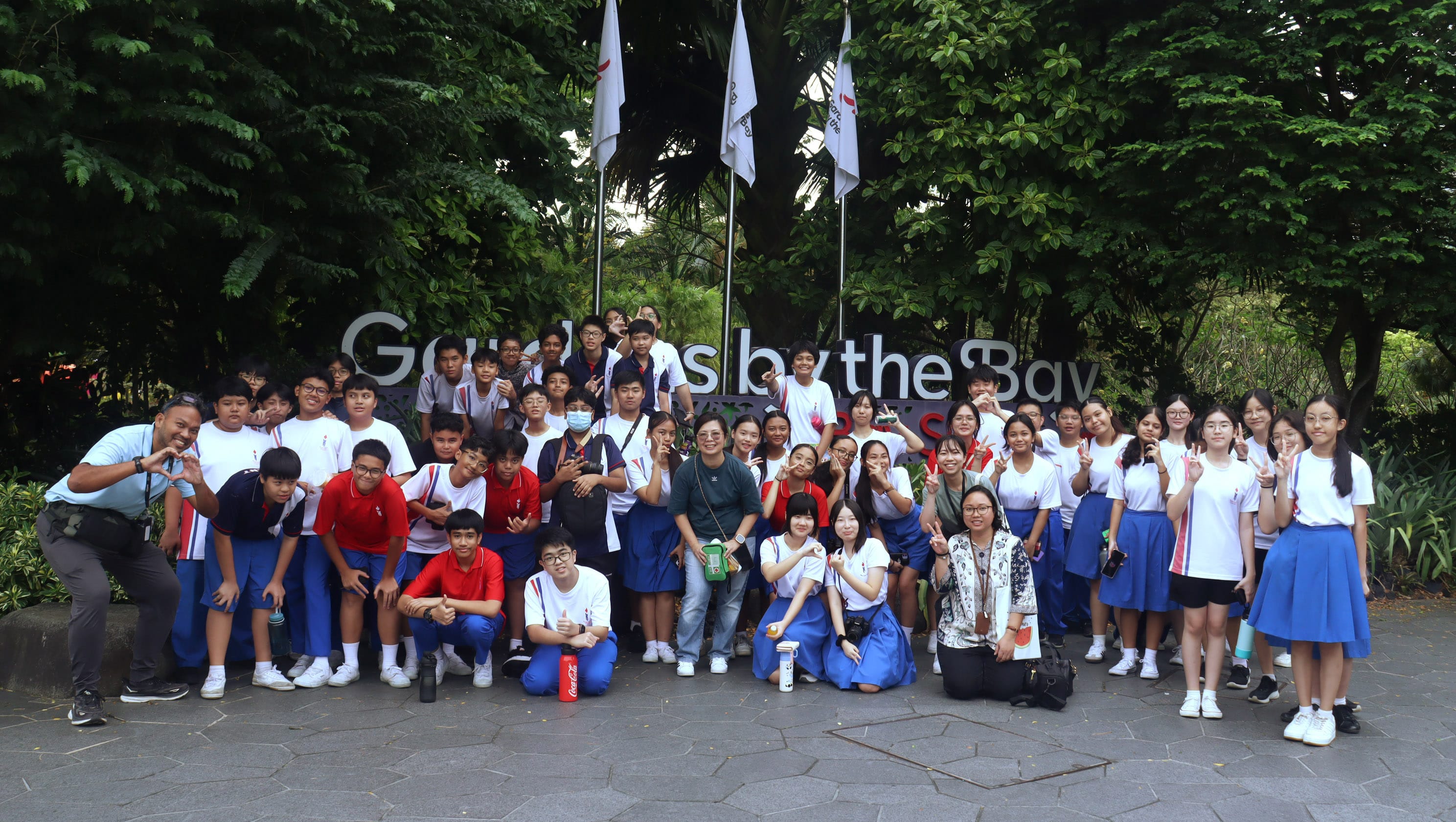 Large group of students in uniforms posing in front of the Gardens by the Bay sign in Singapore.