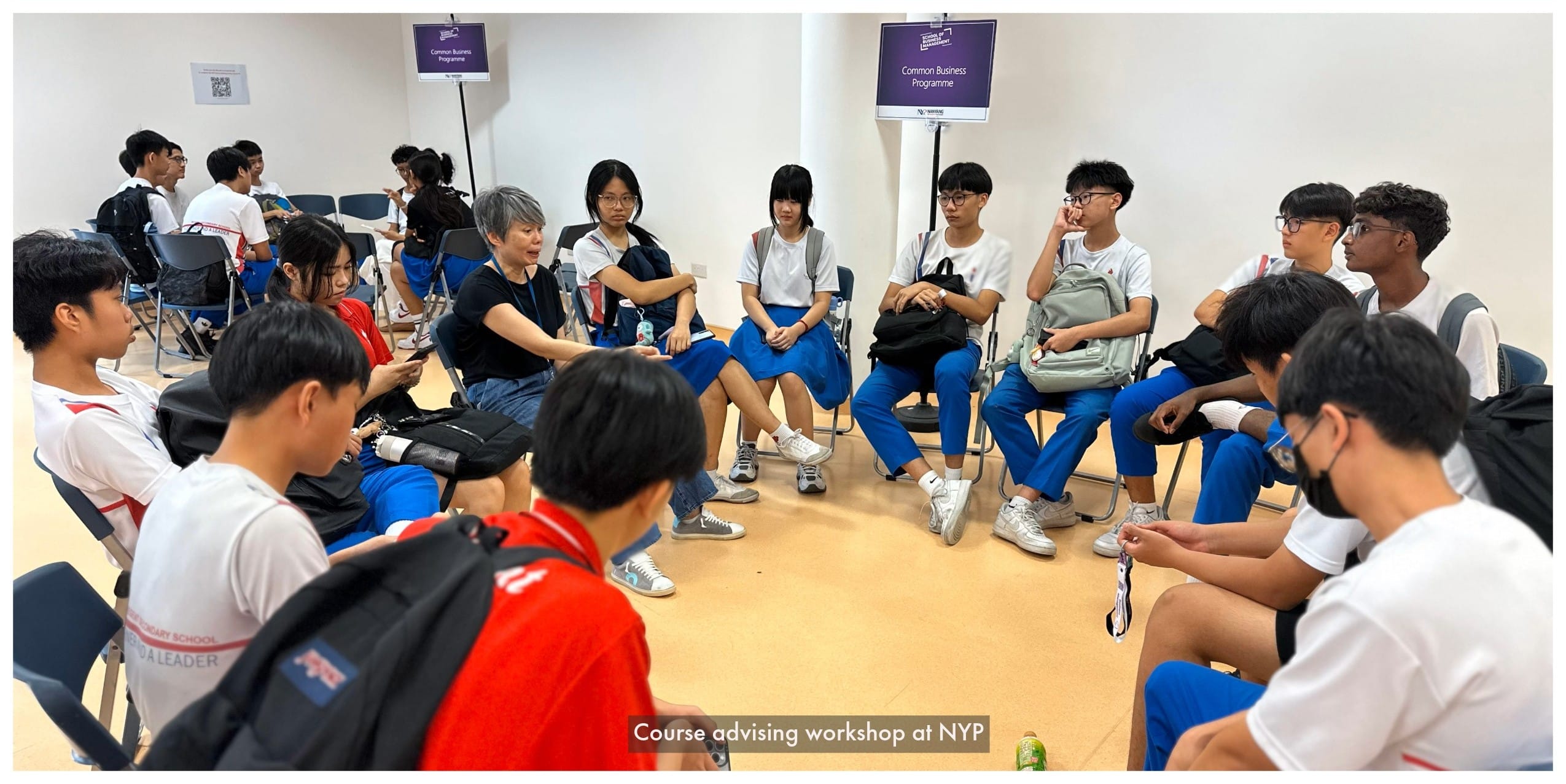 Students in blue uniforms sit in a circle with an adult during a course advising workshop at NYP.