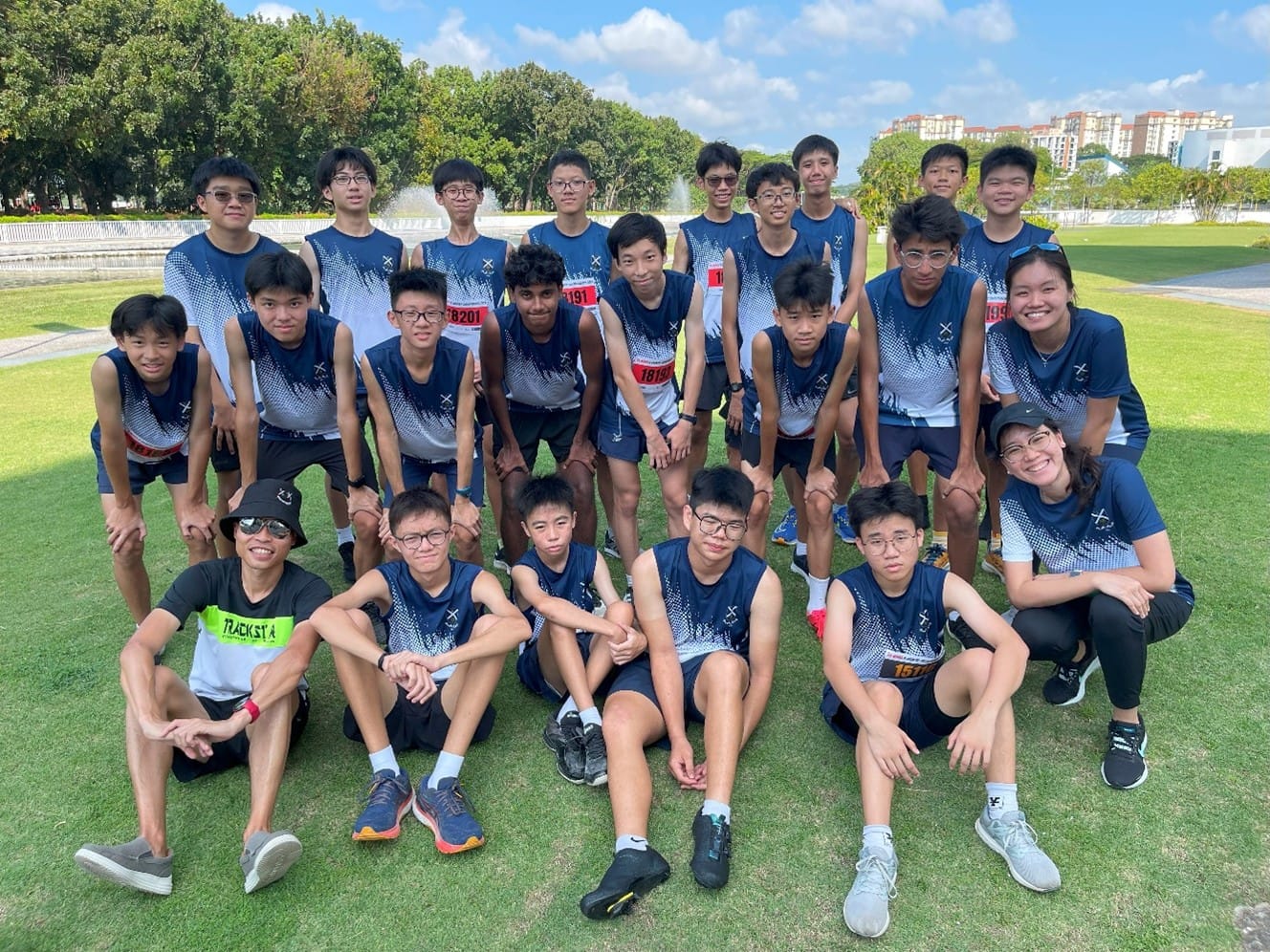 A group of about 25 young runners in matching navy blue jerseys posing together on a grass field outdoors.
