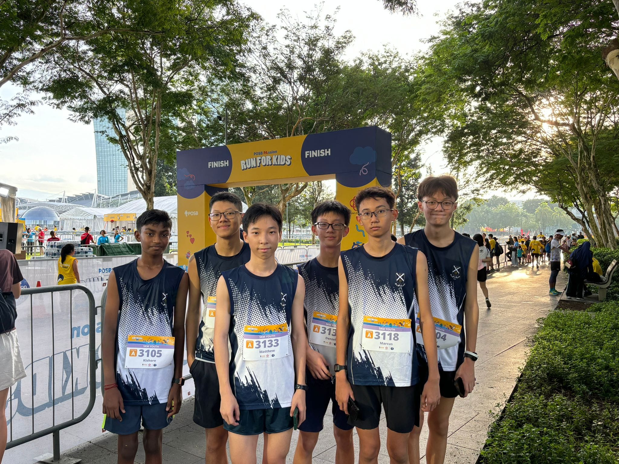 Six young male runners in matching jerseys pose in front of a yellow Run For Kids finish arch.