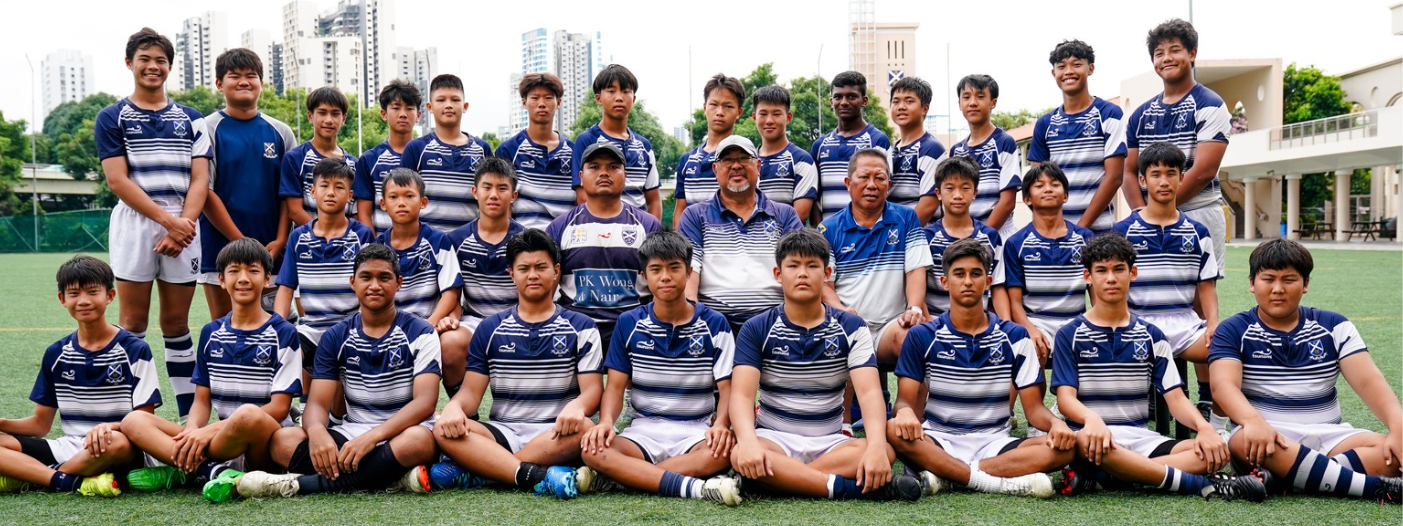 A youth rugby team in navy and white striped jerseys poses with three coaches on a grass field with buildings behind.