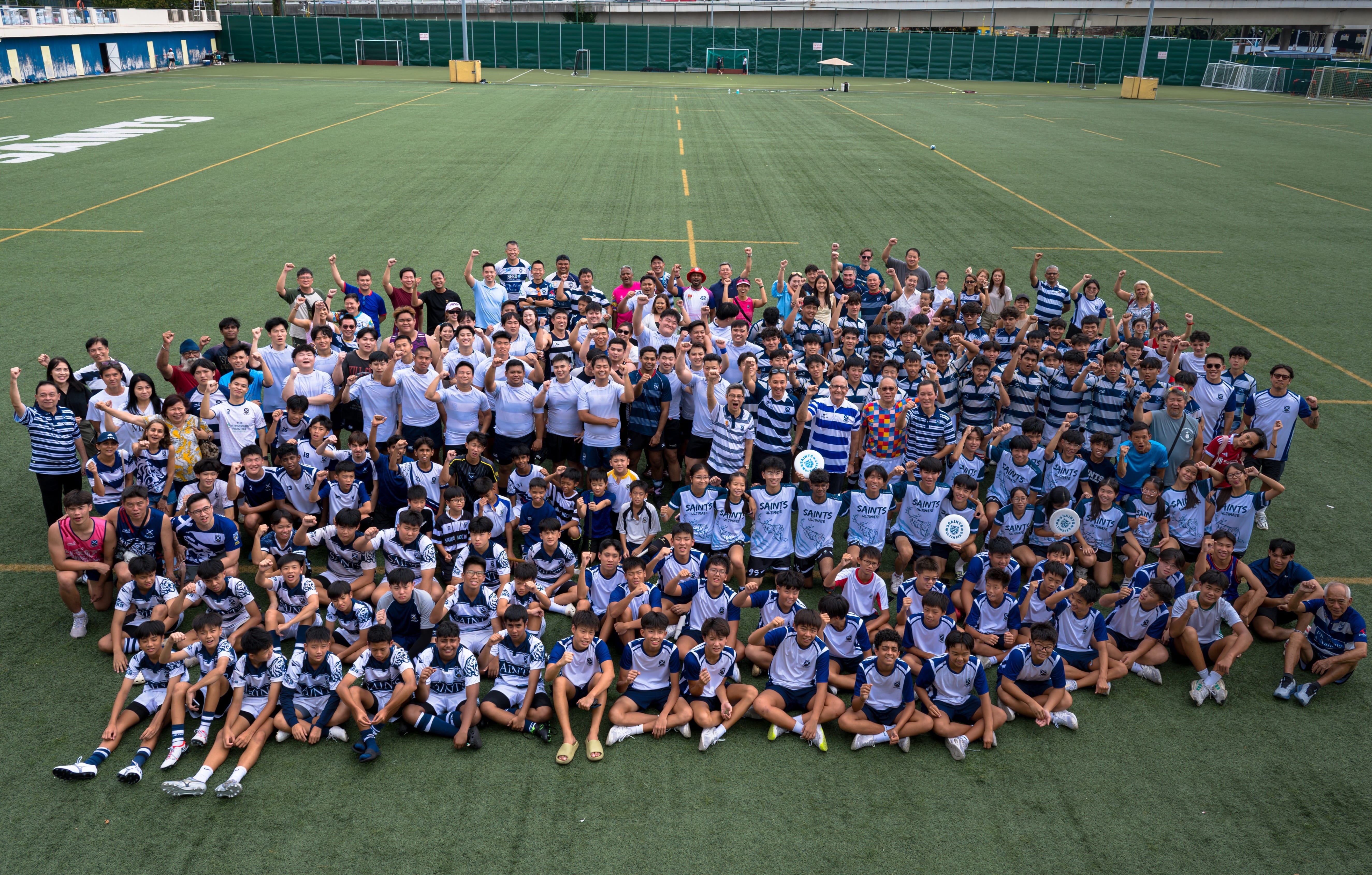 A large group of adults standing behind a large group of students sitting on a field