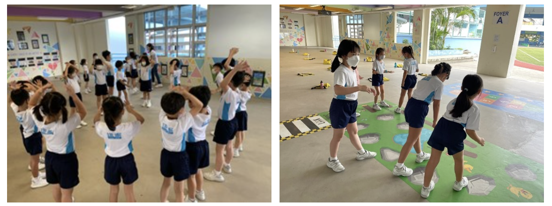 Students in white and blue uniforms do exercises indoors; others step on a colorful floor mat in a covered area.