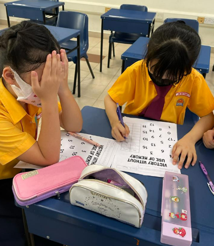 Two students at a desk working on a number worksheet in a classroom.