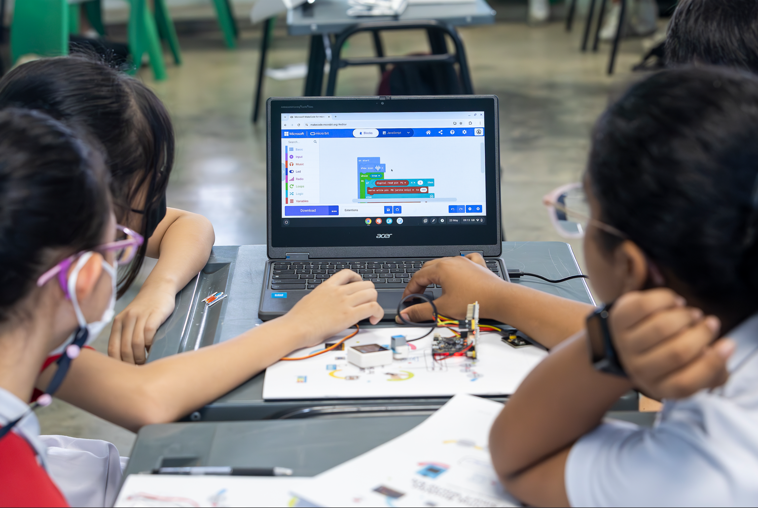 Three children gather around an Acer laptop showing Microsoft MakeCode, with electronic components on the desk.