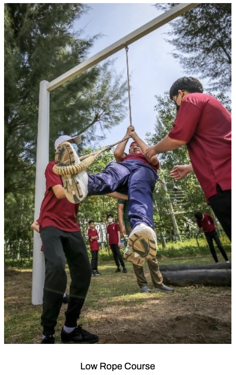 Our students swings on a rope while two others in red shirts assist during a low rope course activity at our Sec 1 Outdoor Adventure Learning Camp.