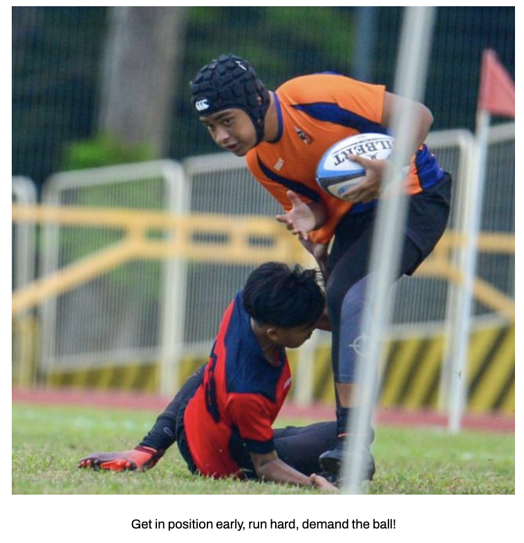A rugby player in orange holds a ball while stepping over a tackled opponent in red on the grass field.