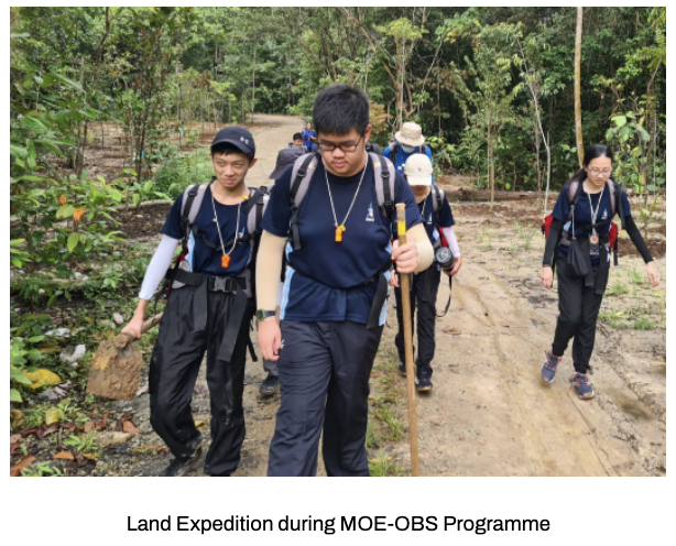 Our students with backpacks hiking along a dirt trail through a forest during an MOE-OBS land expedition.