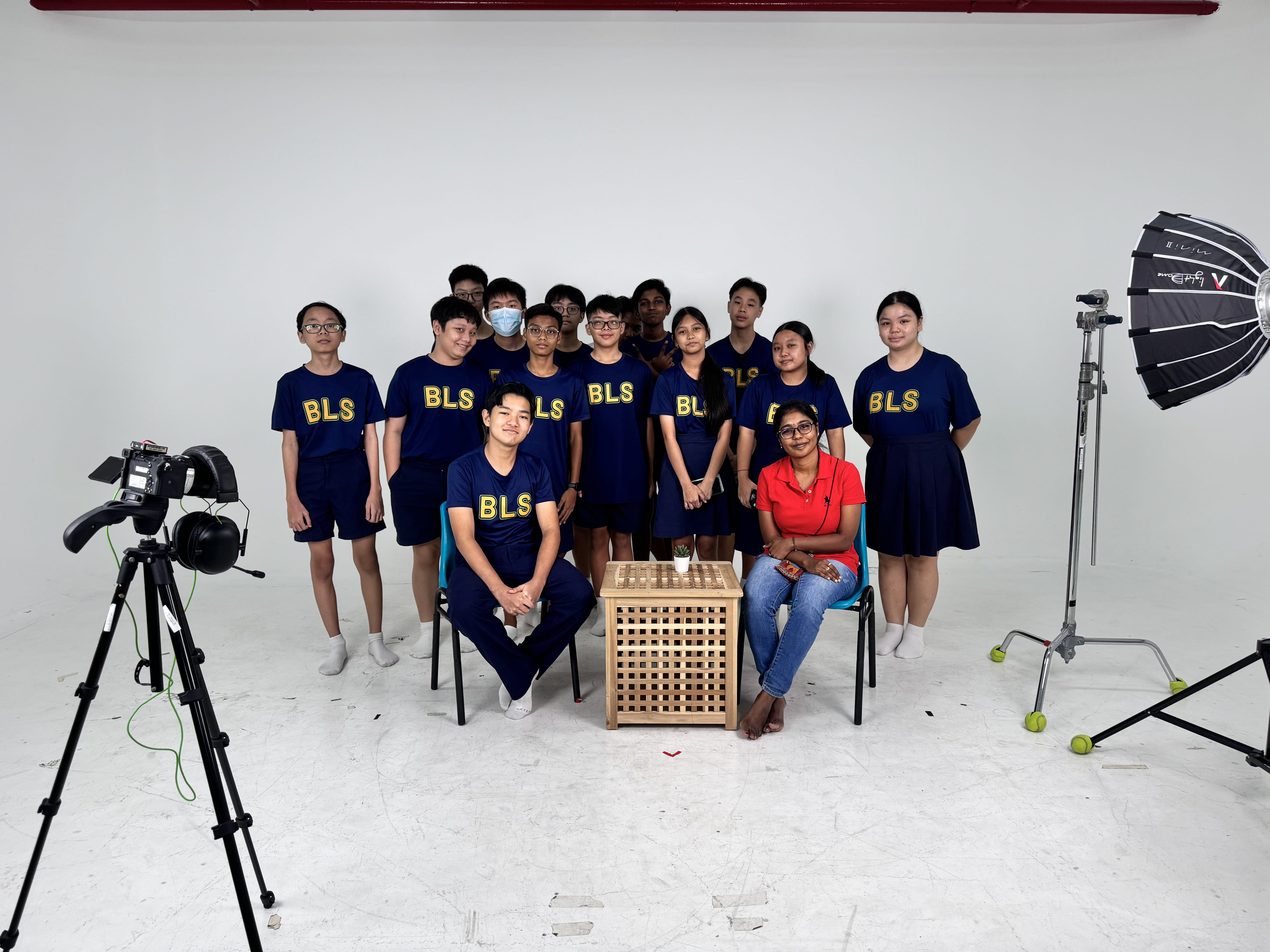 Group of students in navy BLS shirts posing in a photography studio with camera and softbox lighting equipment.