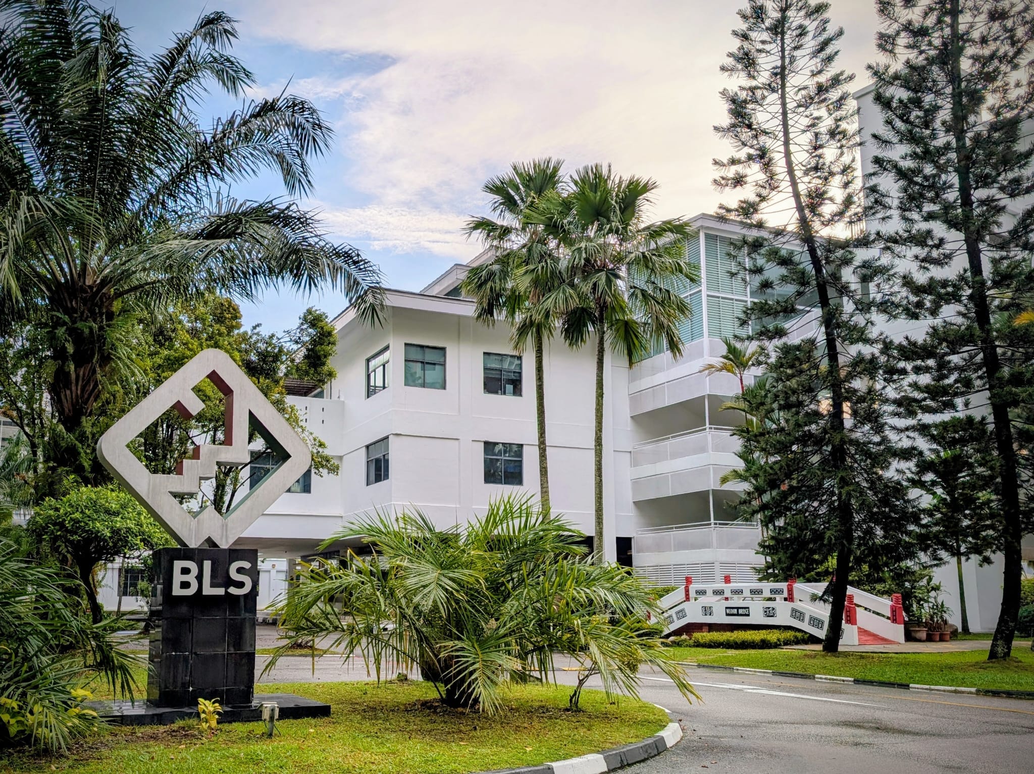 A white multi-story building with a BLS sign and diamond sculpture at the entrance, surrounded by palm trees.