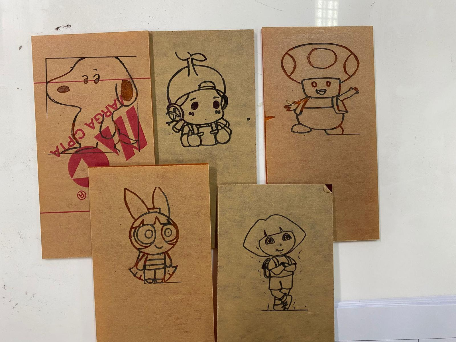 Five brown cardboard pieces with hand-drawn cartoon characters including Snoopy, Toad, Dora, and Powerpuff Girls.