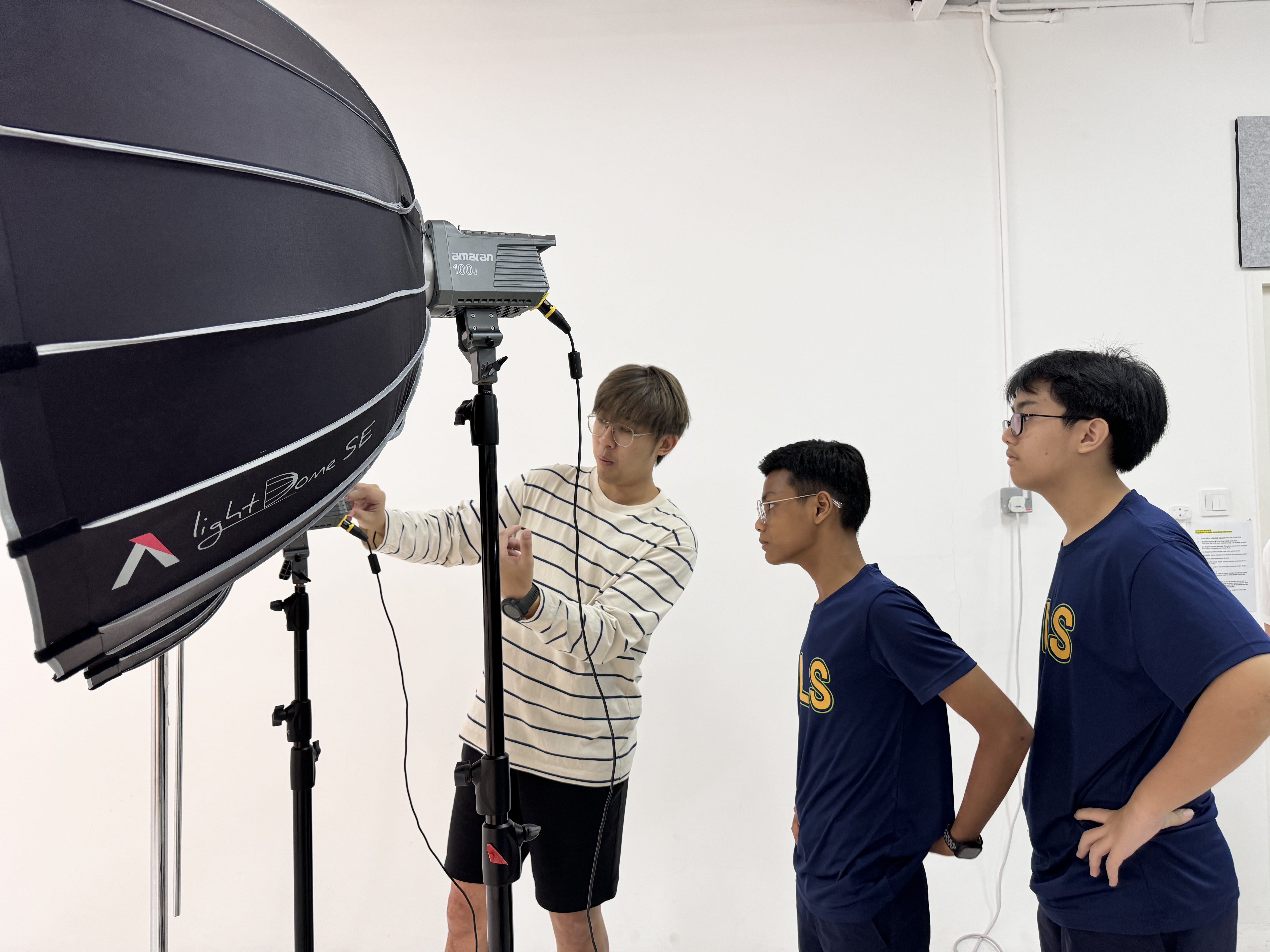 Three young men in a white studio examining a large Amaran Light Dome SE softbox on a stand.