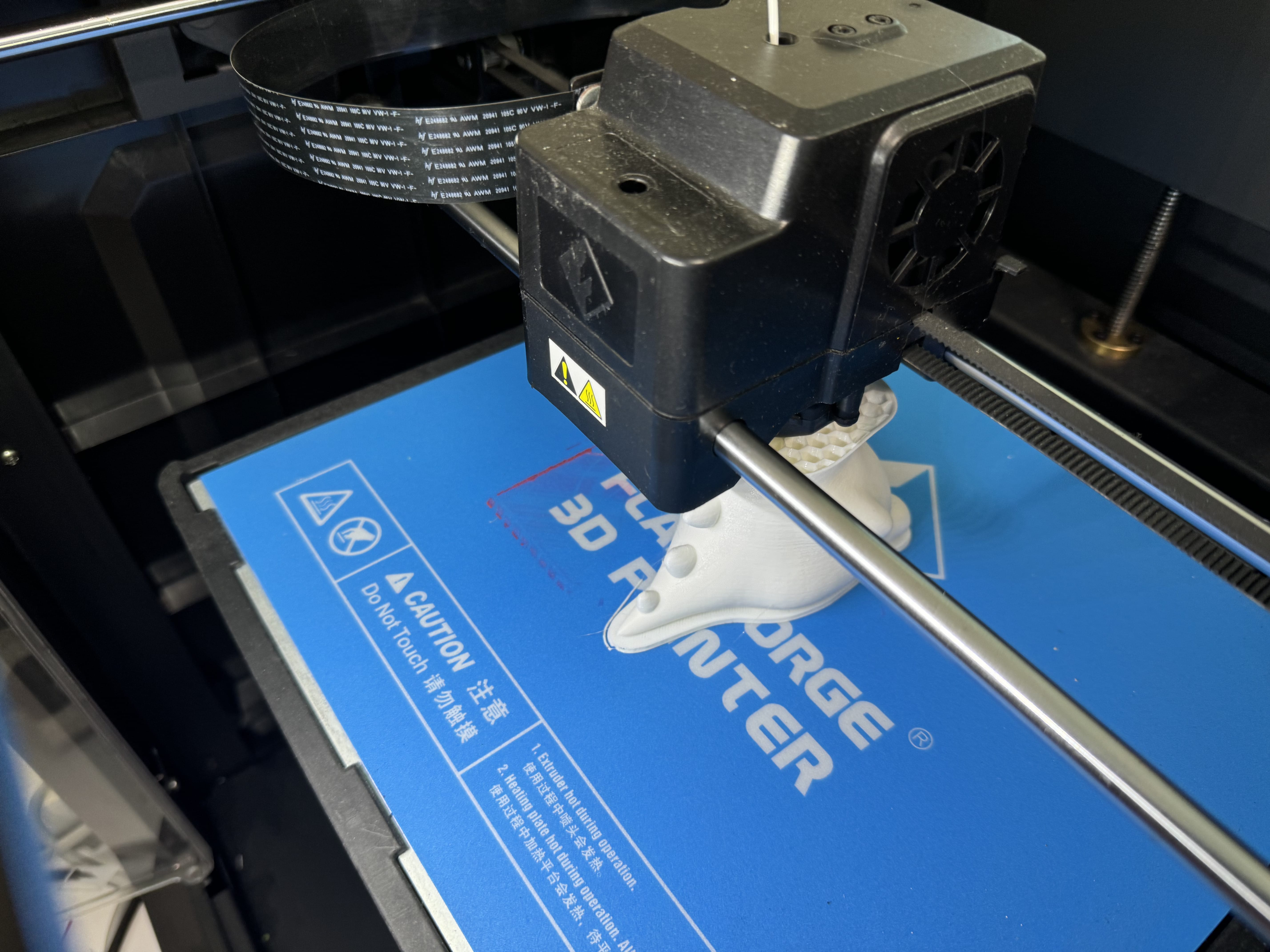 A 3D printer actively printing a small white object on a blue build plate.