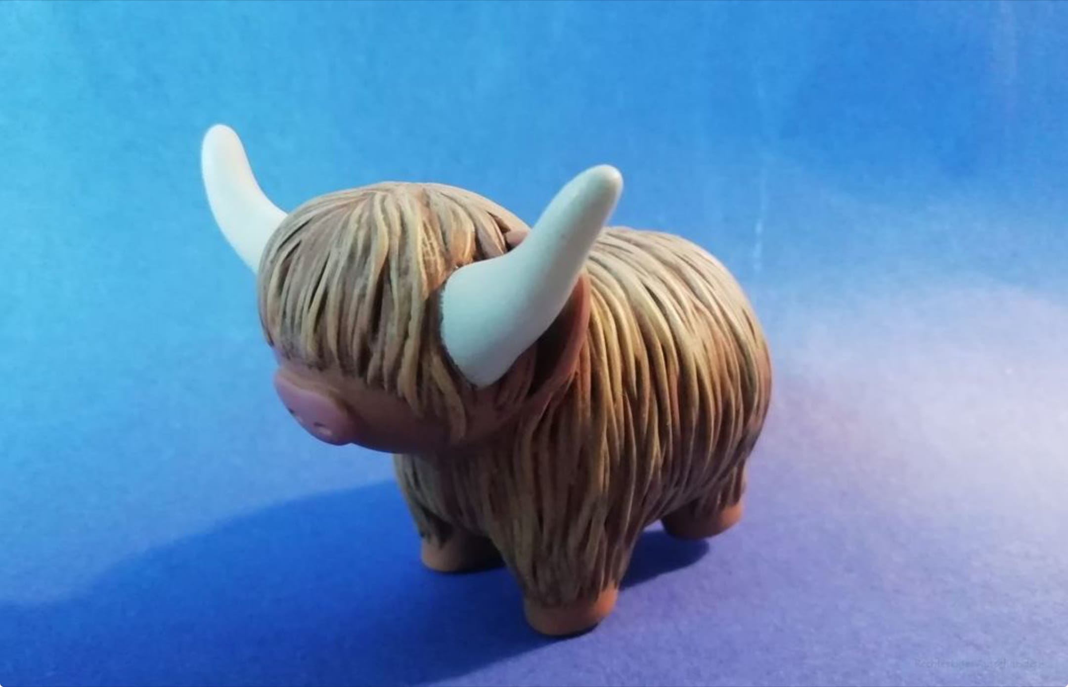 Small brown highland cow figurine with long shaggy fur and two white horns on a blue background.