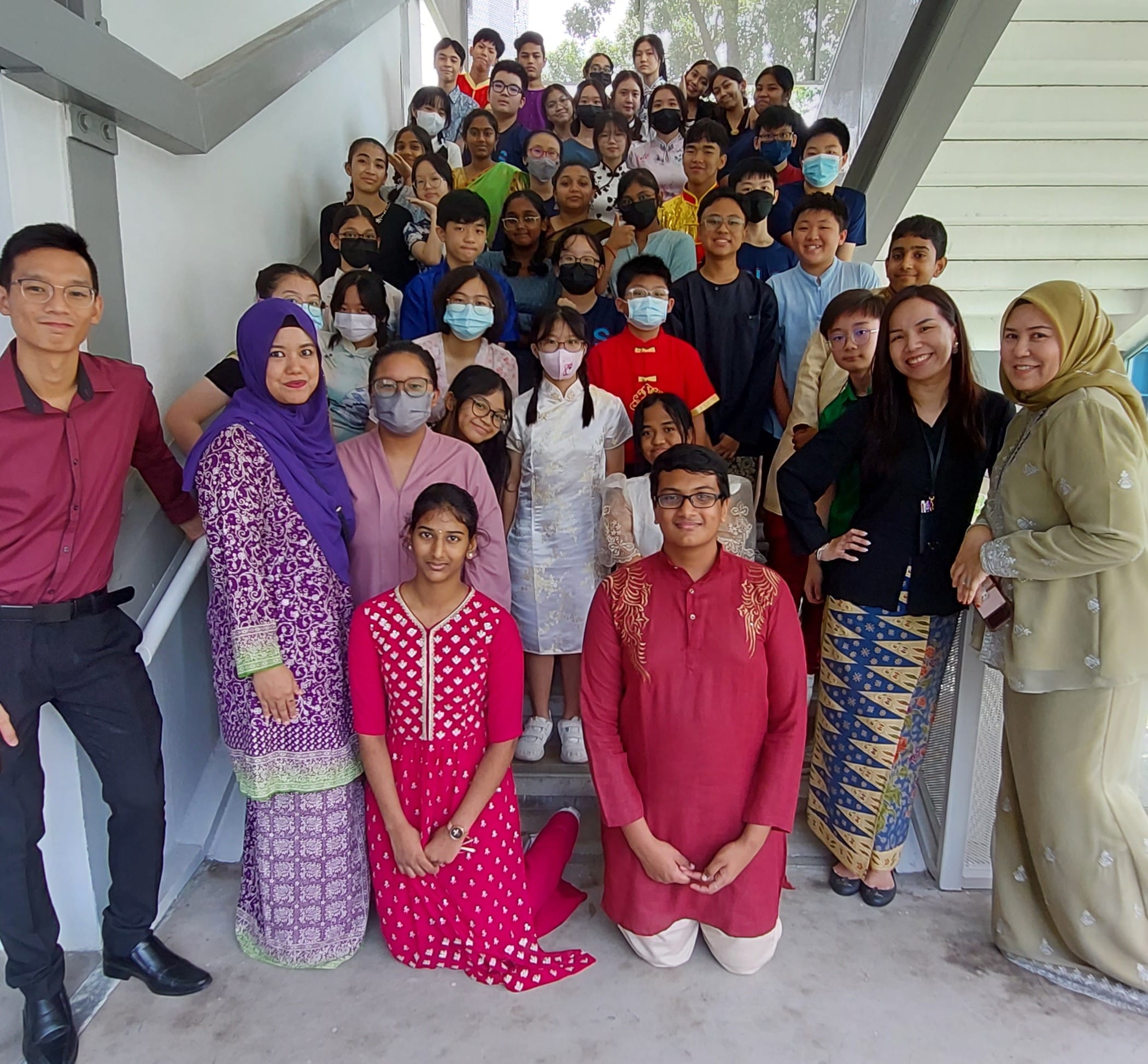 A large diverse group of students and teachers in traditional cultural attire posing on a staircase.