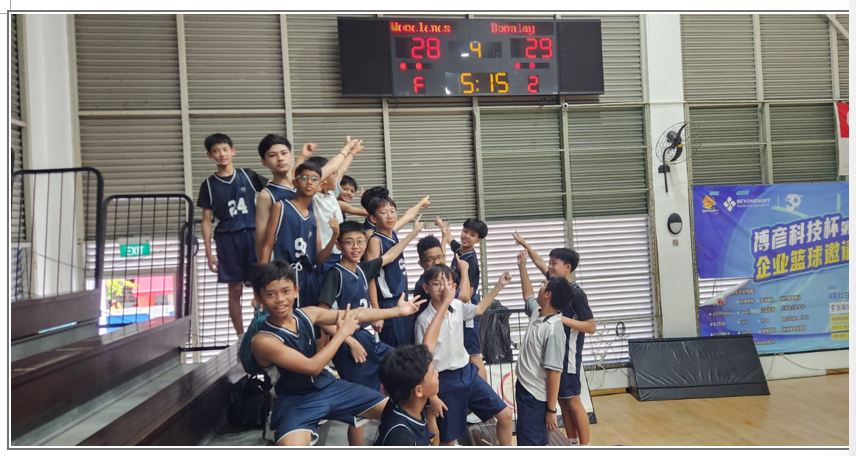 A group of young basketball players in navy uniforms pose and cheer under a scoreboard showing 28-29.