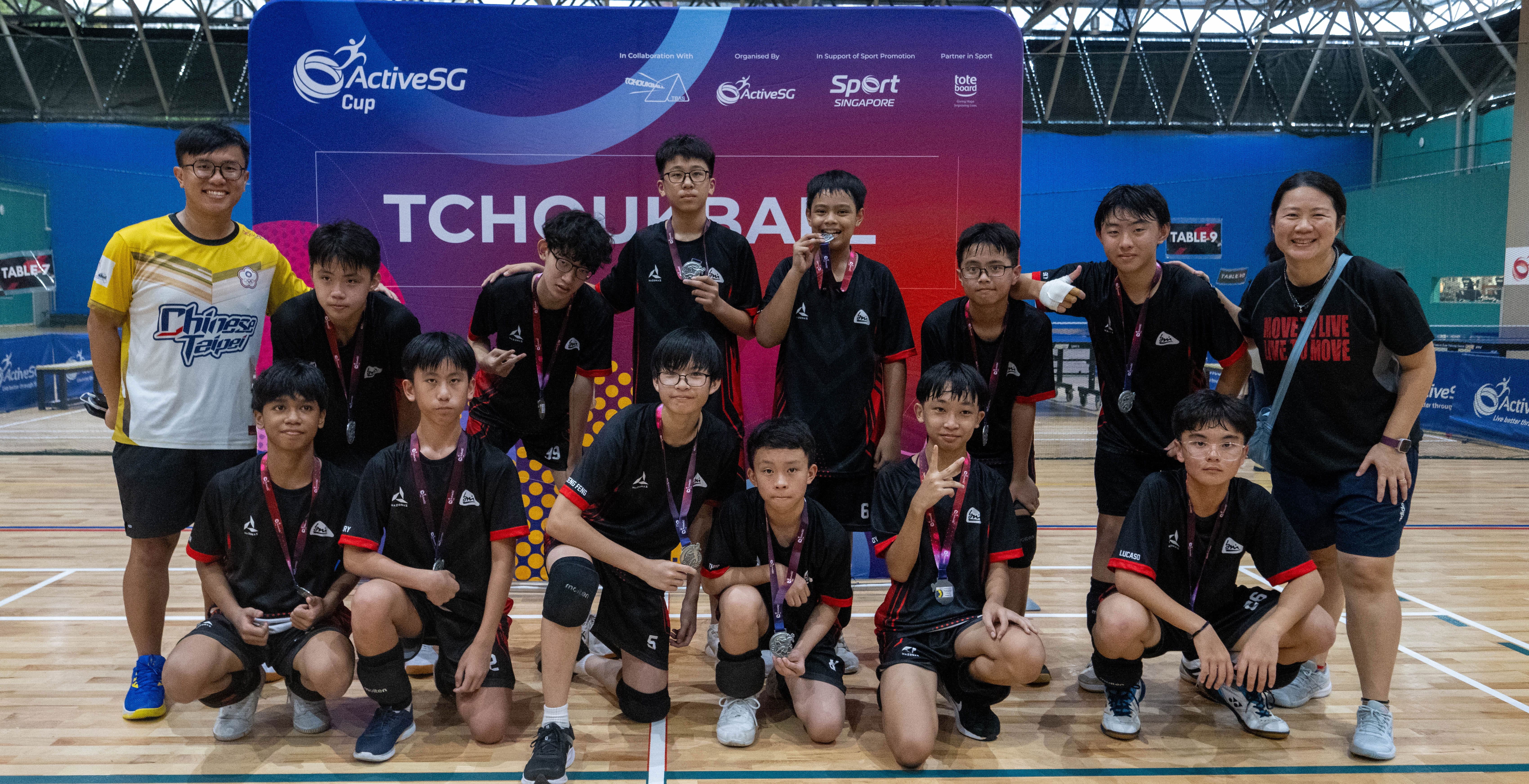 Youth table tennis team in black uniforms pose with medals before an ActiveSG Cup photo backdrop.