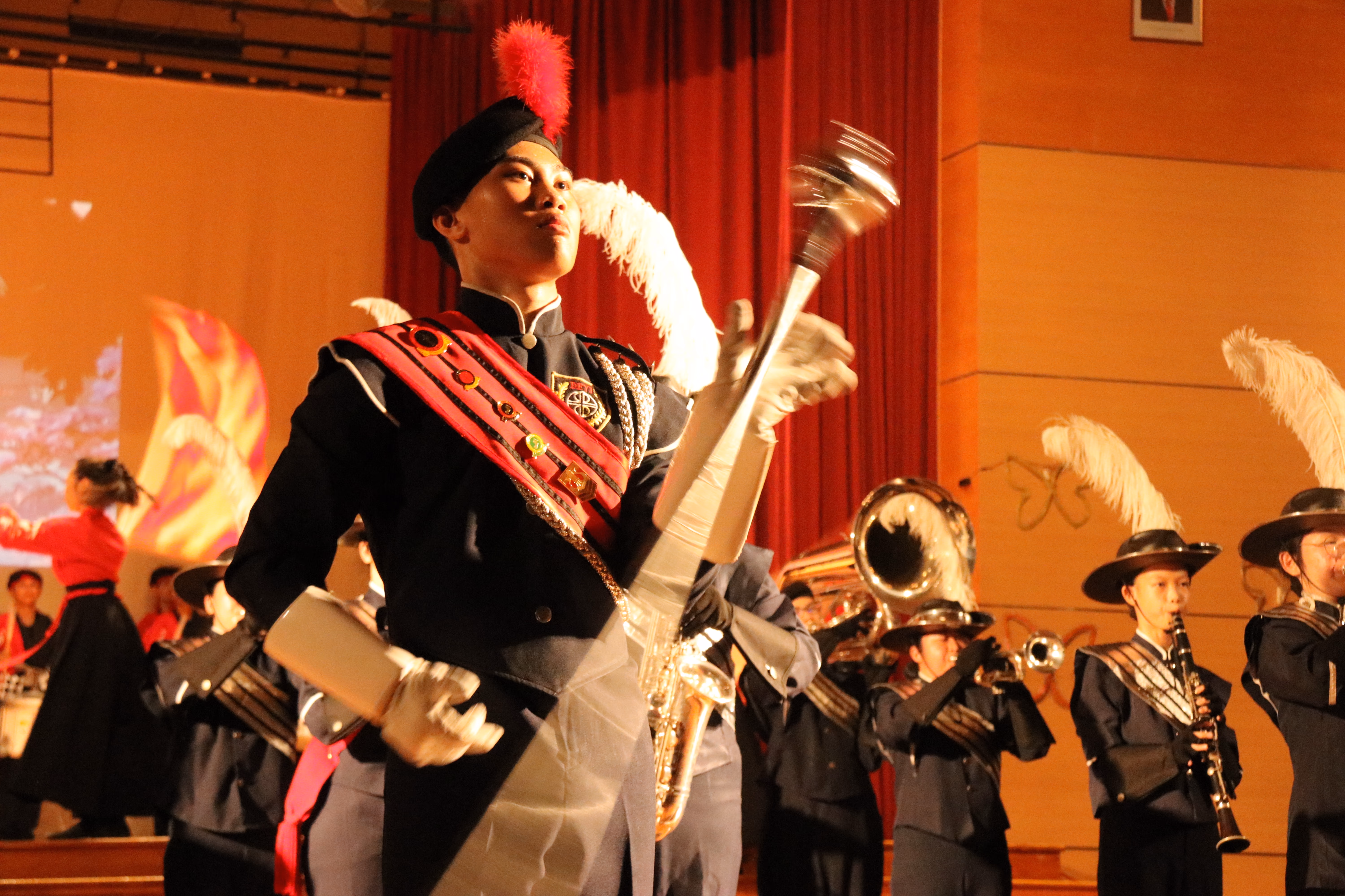 Student drum major twirling a mace while the school band performs on stage.