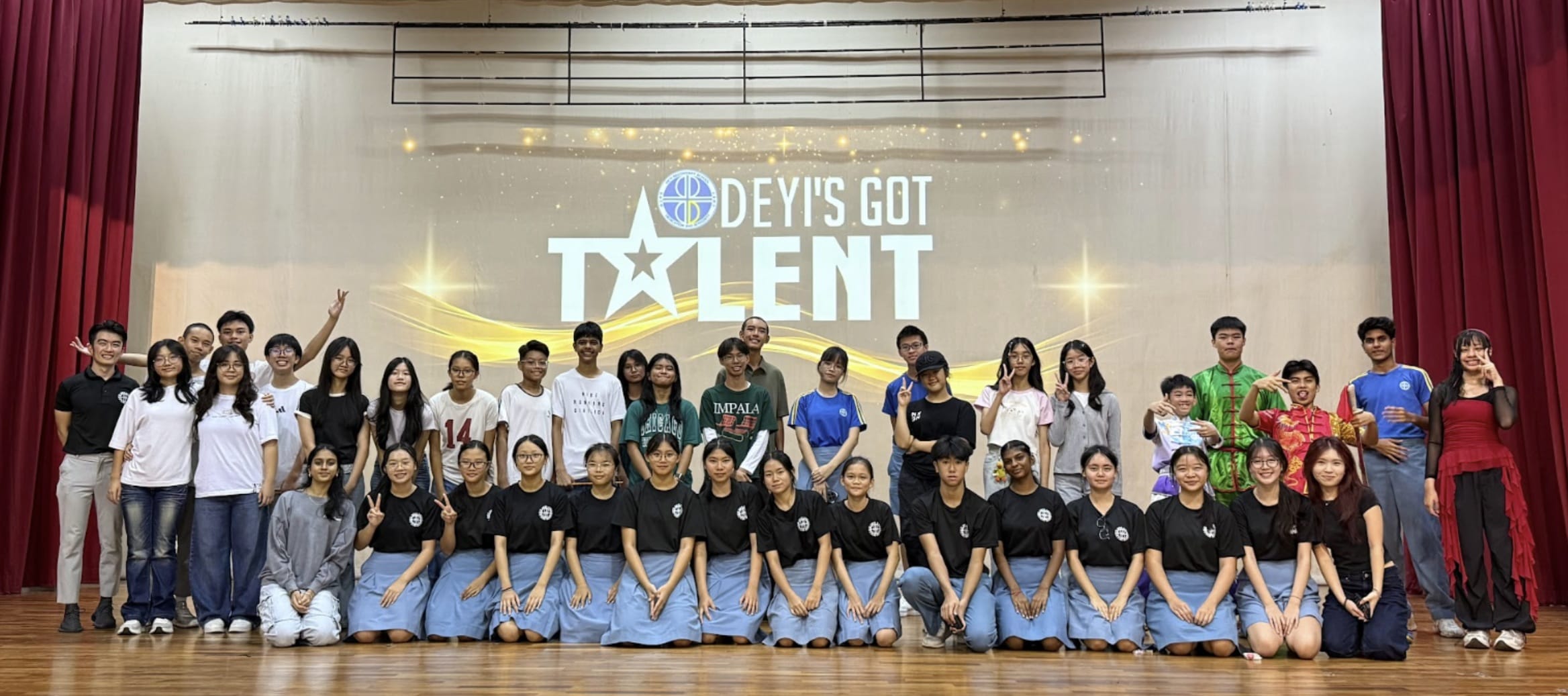 A large group of students pose on a stage in front of a backdrop reading Deyi's Got Talent.