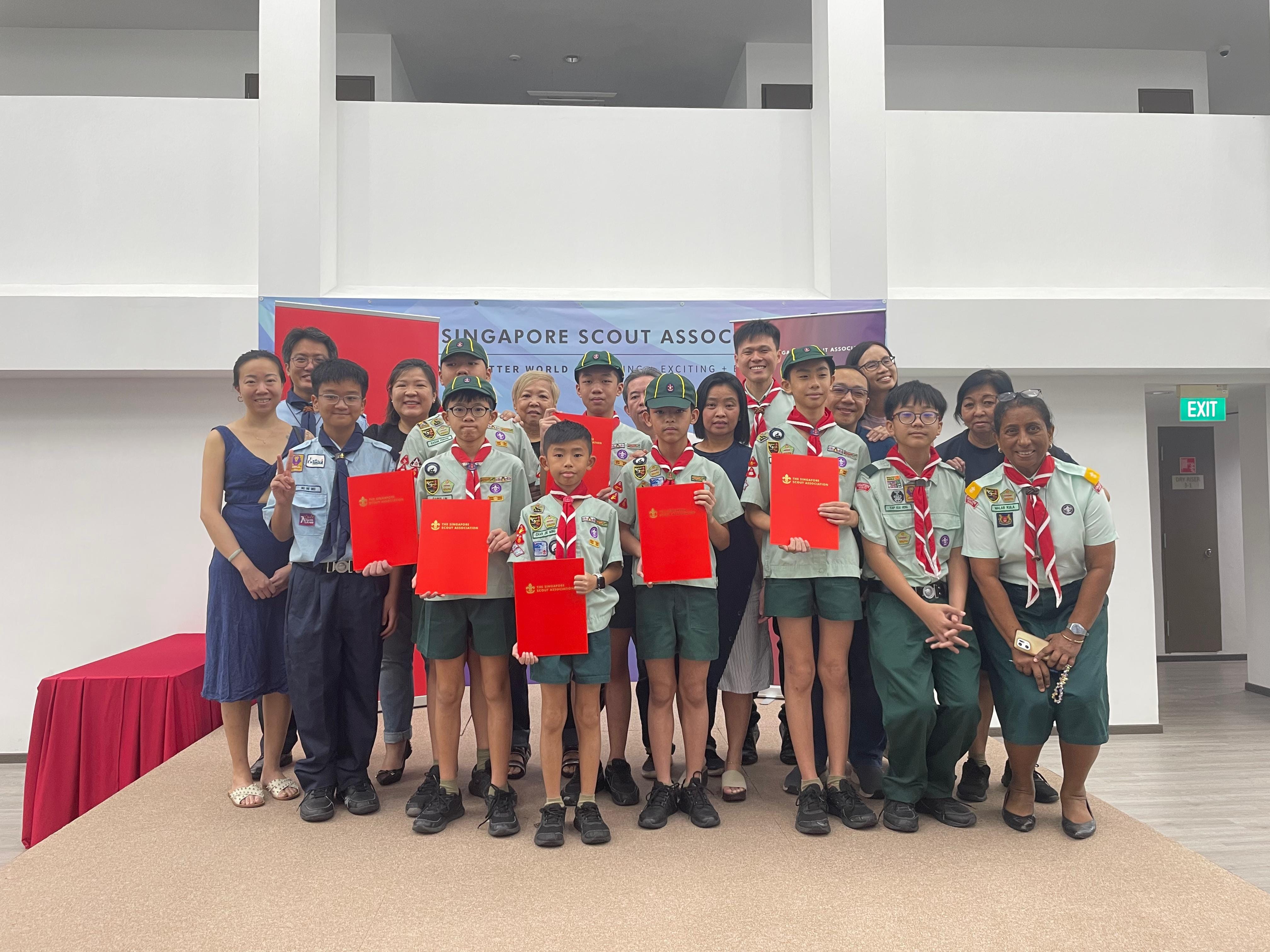 Group of young scouts in uniform holding red certificates at a Singapore Scout Association award ceremony.