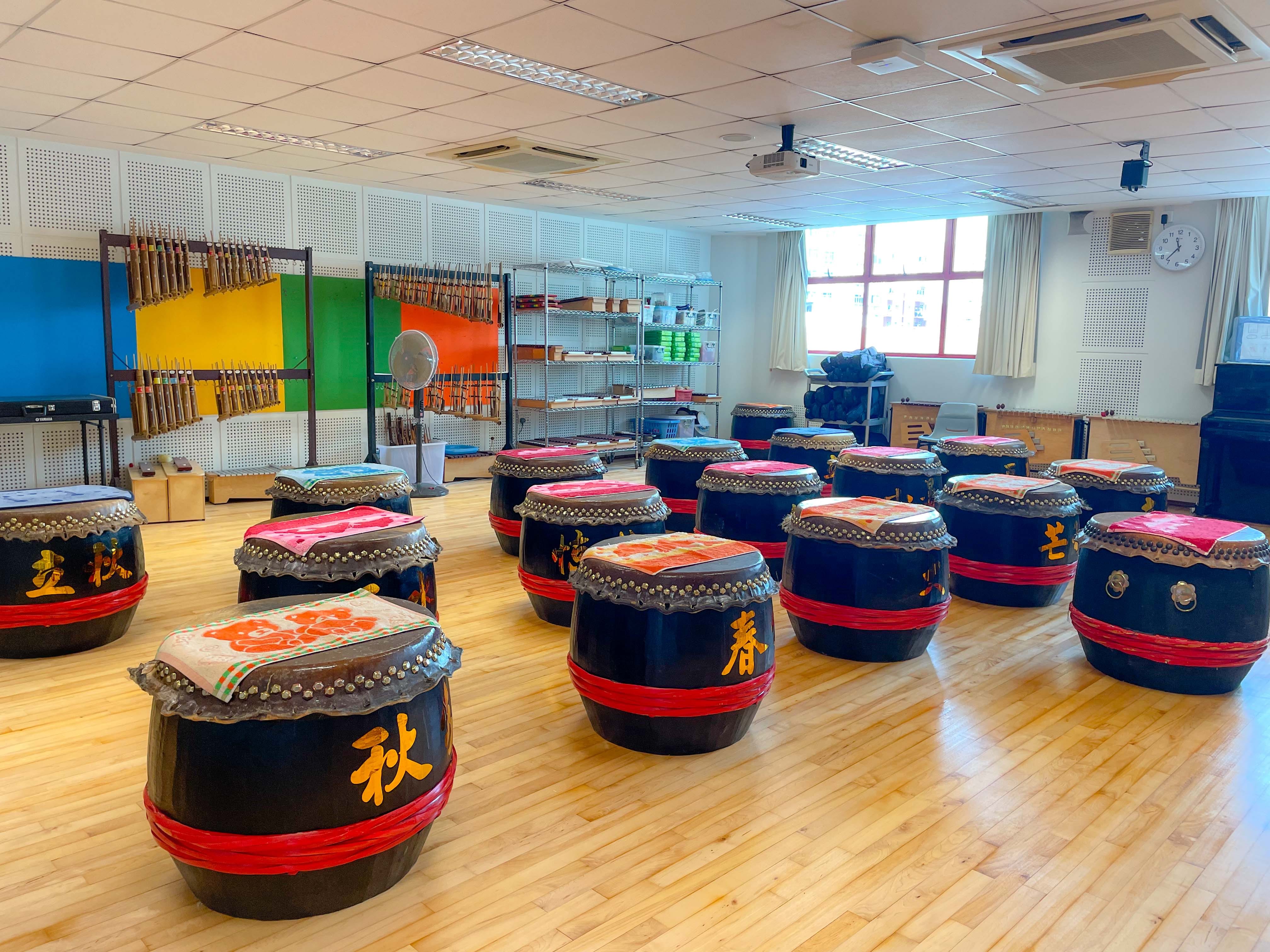 A room filled with large black Chinese drums with red bands and gold characters on a wooden floor.