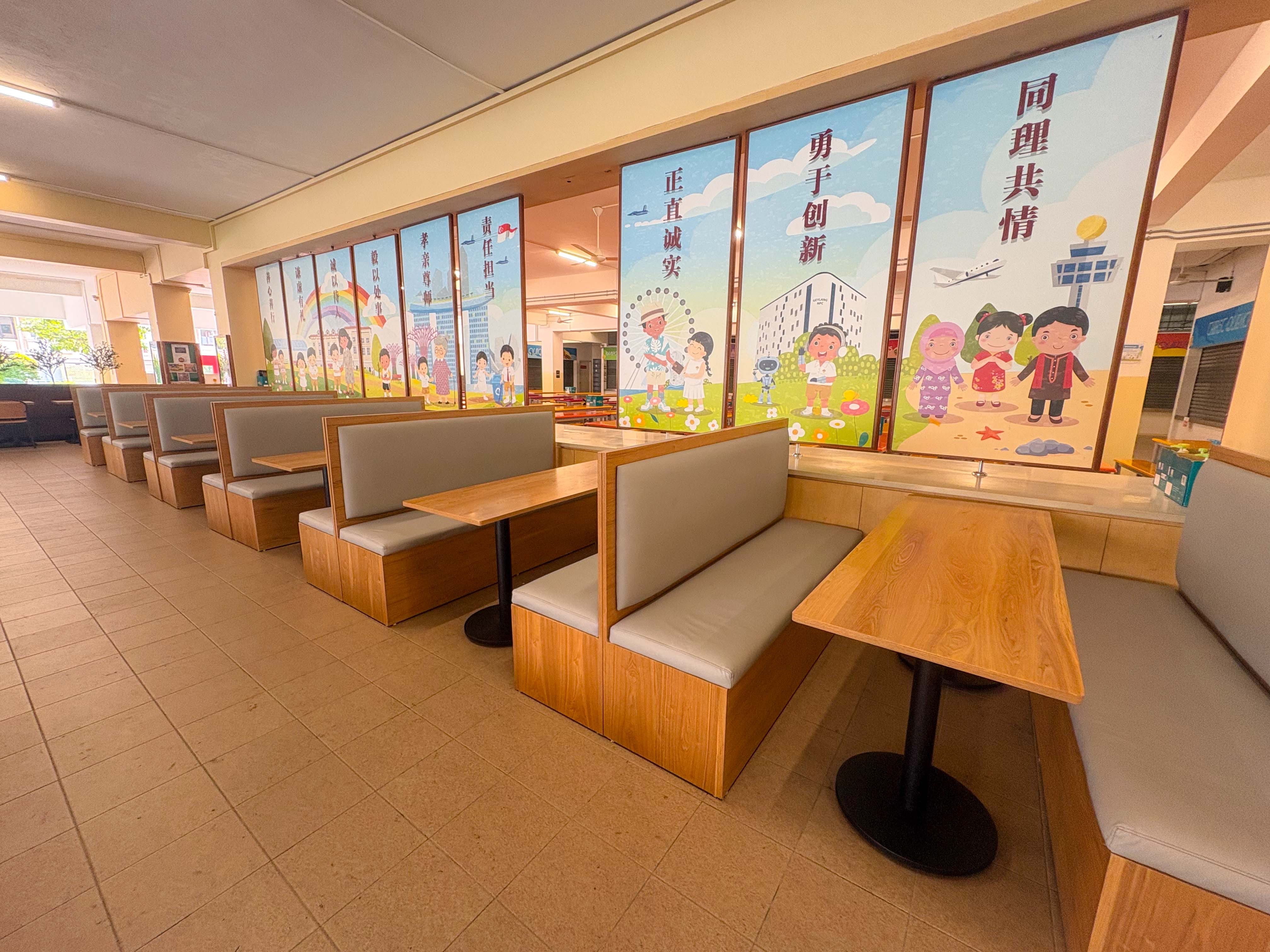 Empty school cafeteria with rows of orange tables and benches, colorful Chinese character banners on walls and windows.