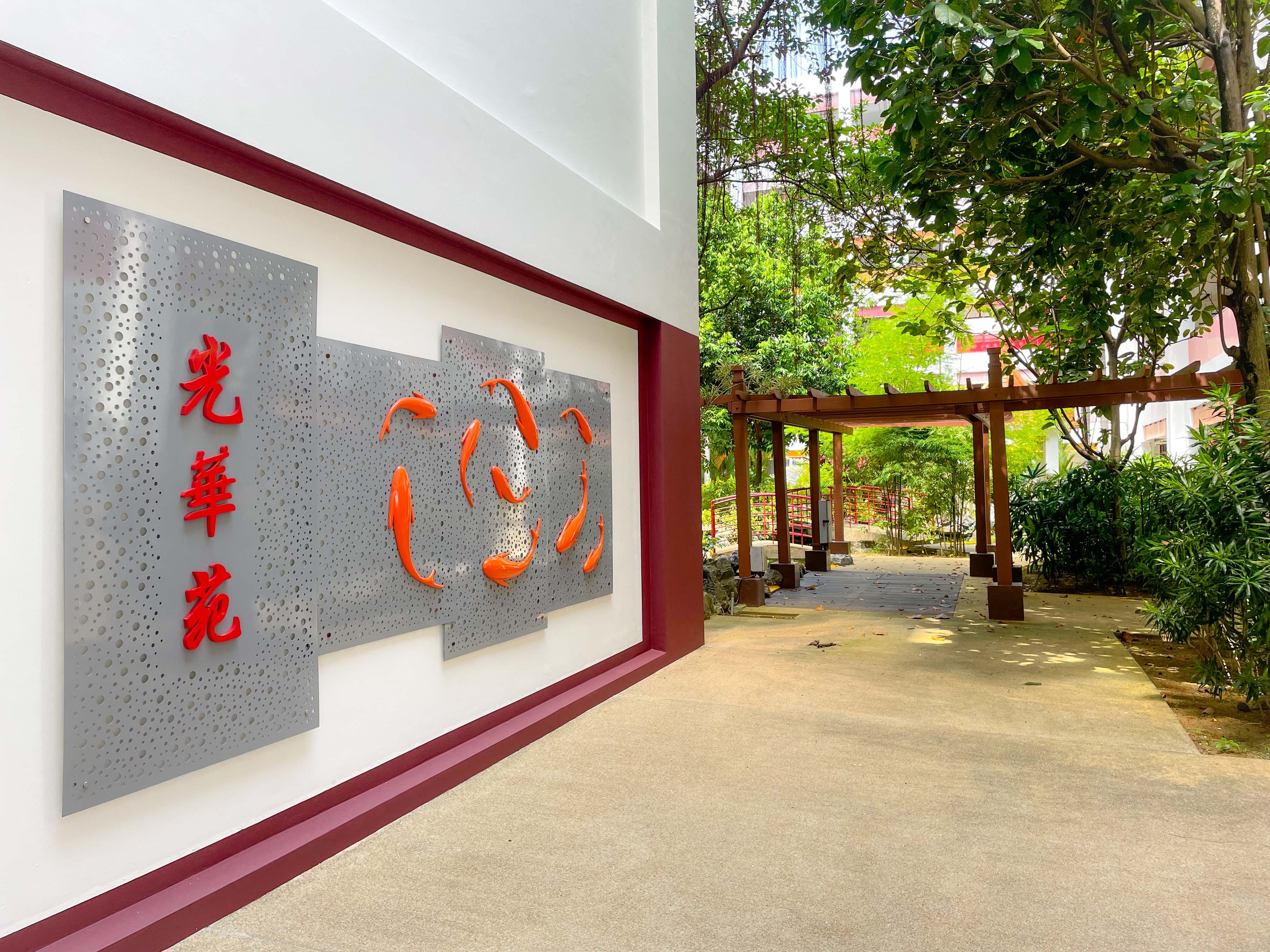Wall mural with red Chinese characters and orange koi fish beside a garden path leading to a wooden pergola.