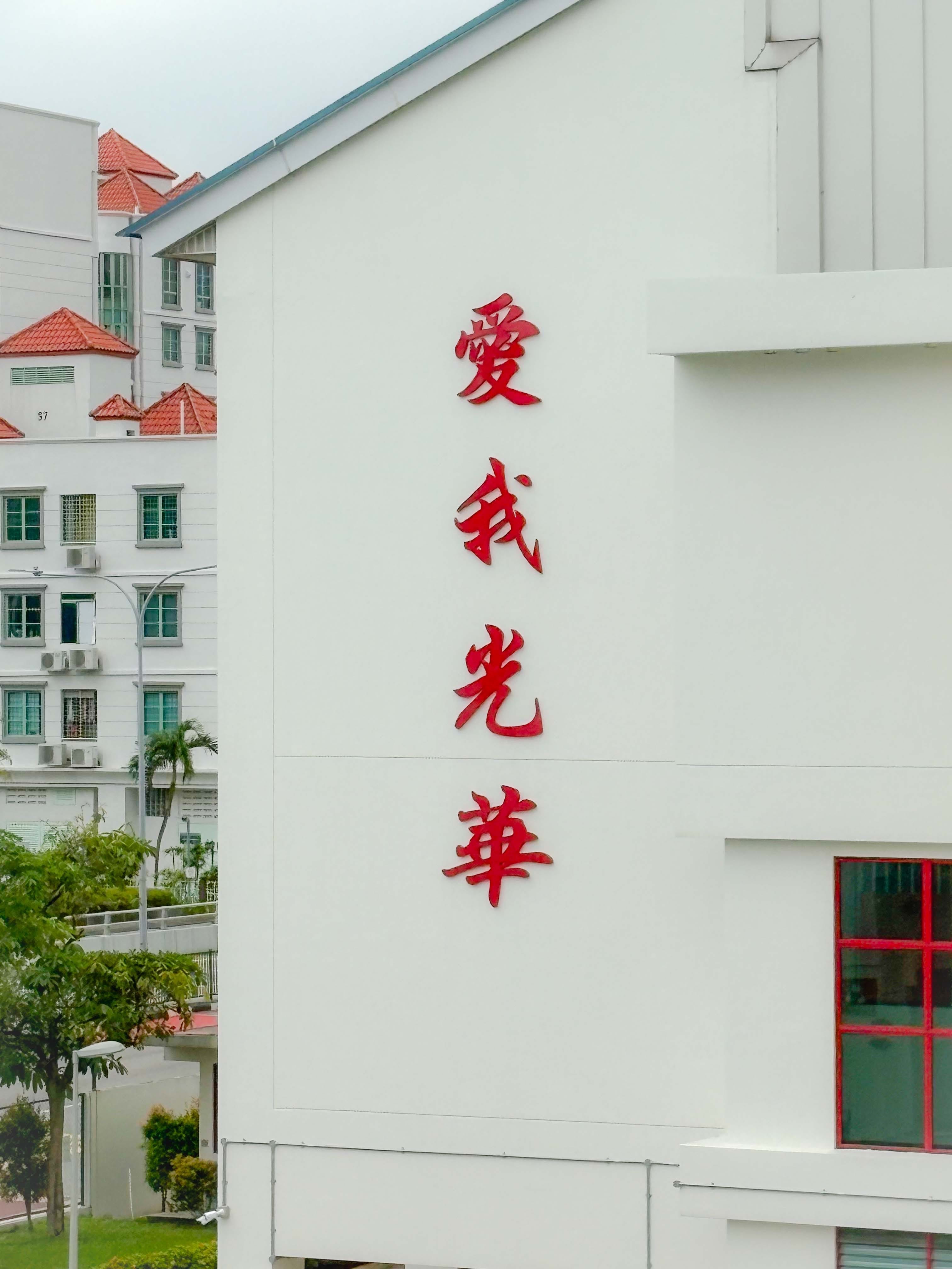 Four red Chinese characters mounted vertically on a white building wall, with residential blocks visible in the background.