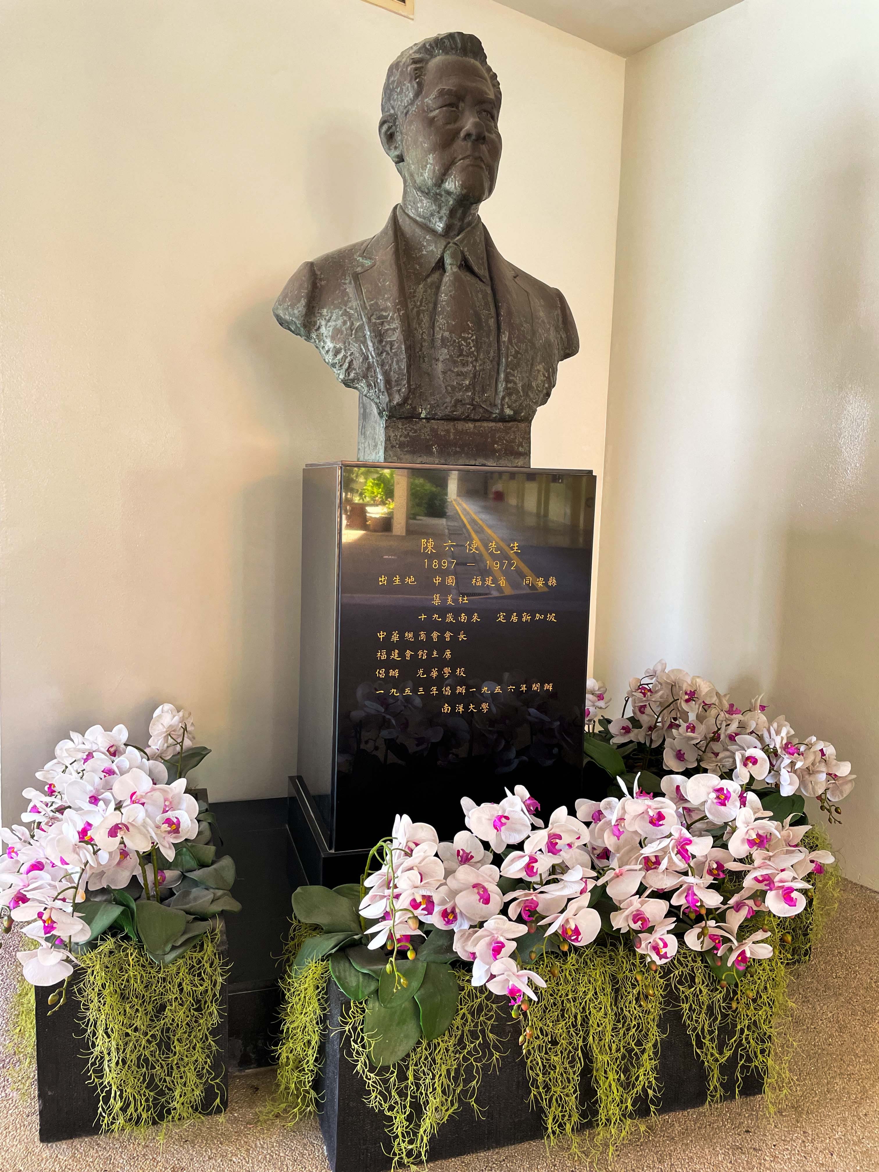 Bronze bust of a man on a dark plaque with Chinese text dated 1897-1972, surrounded by white and pink orchid arrangements.
