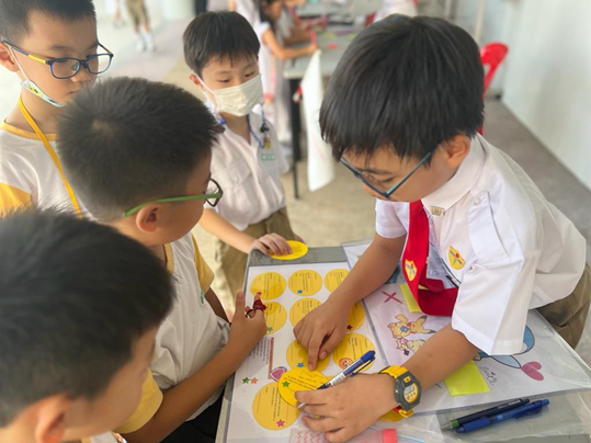 Four young students in uniforms collaborate on a poster with yellow circle cutouts on a table.